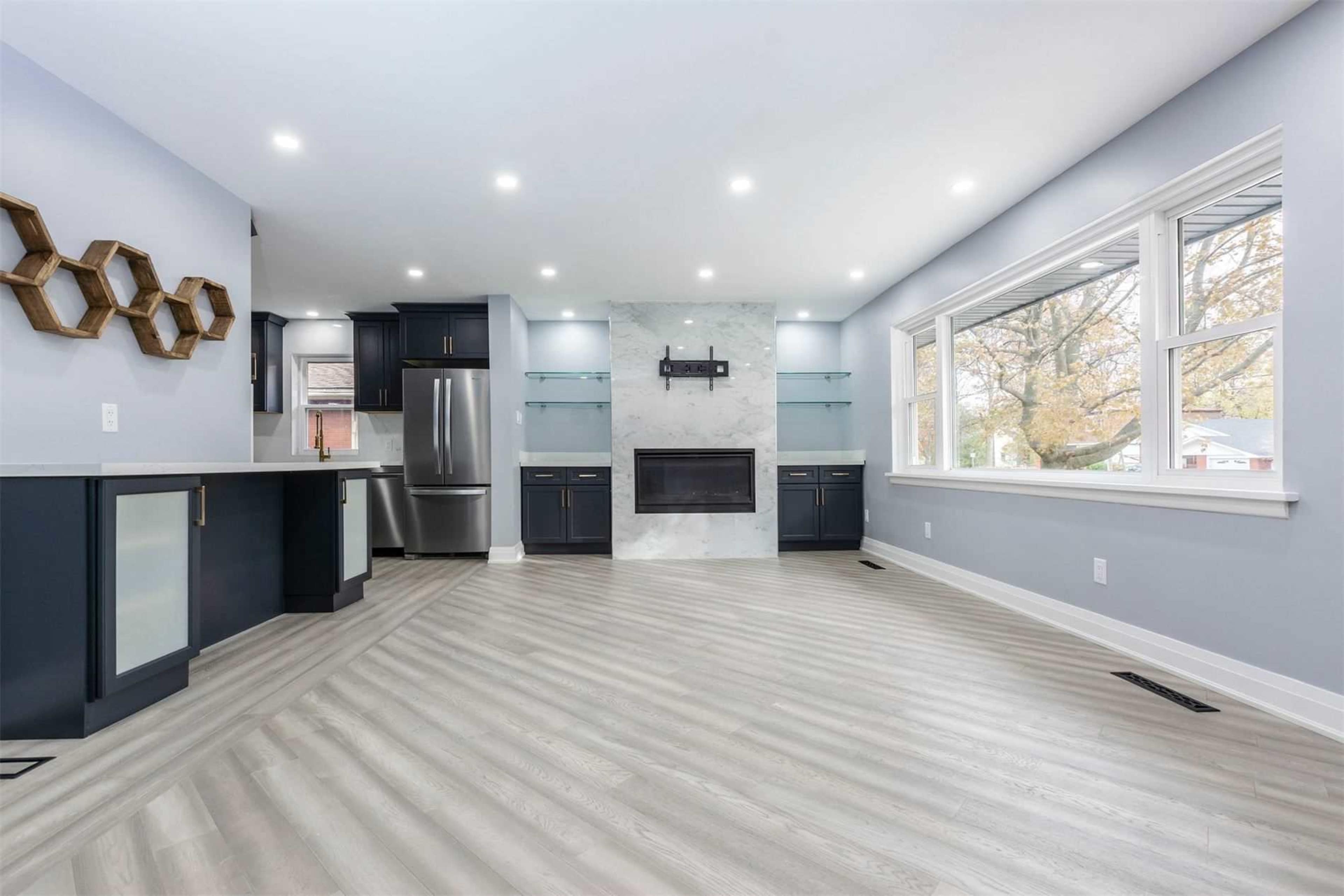 The image shows a modern living room featuring a fireplace, large windows, and a mix of dark cabinetry and light flooring.