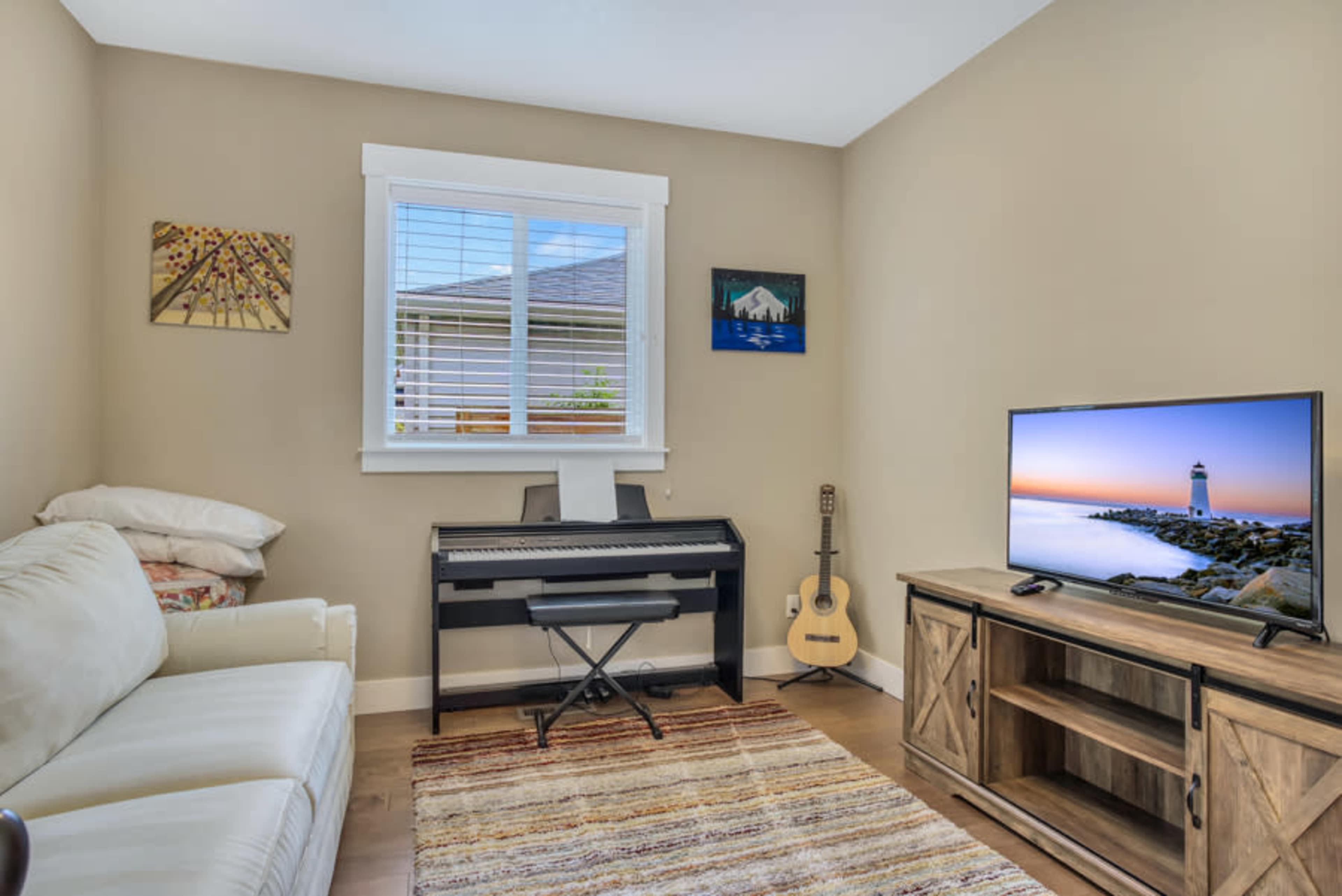 A small room featuring a white sofa, a black piano, a television on a wooden stand, and a guitar leaning against the wall.