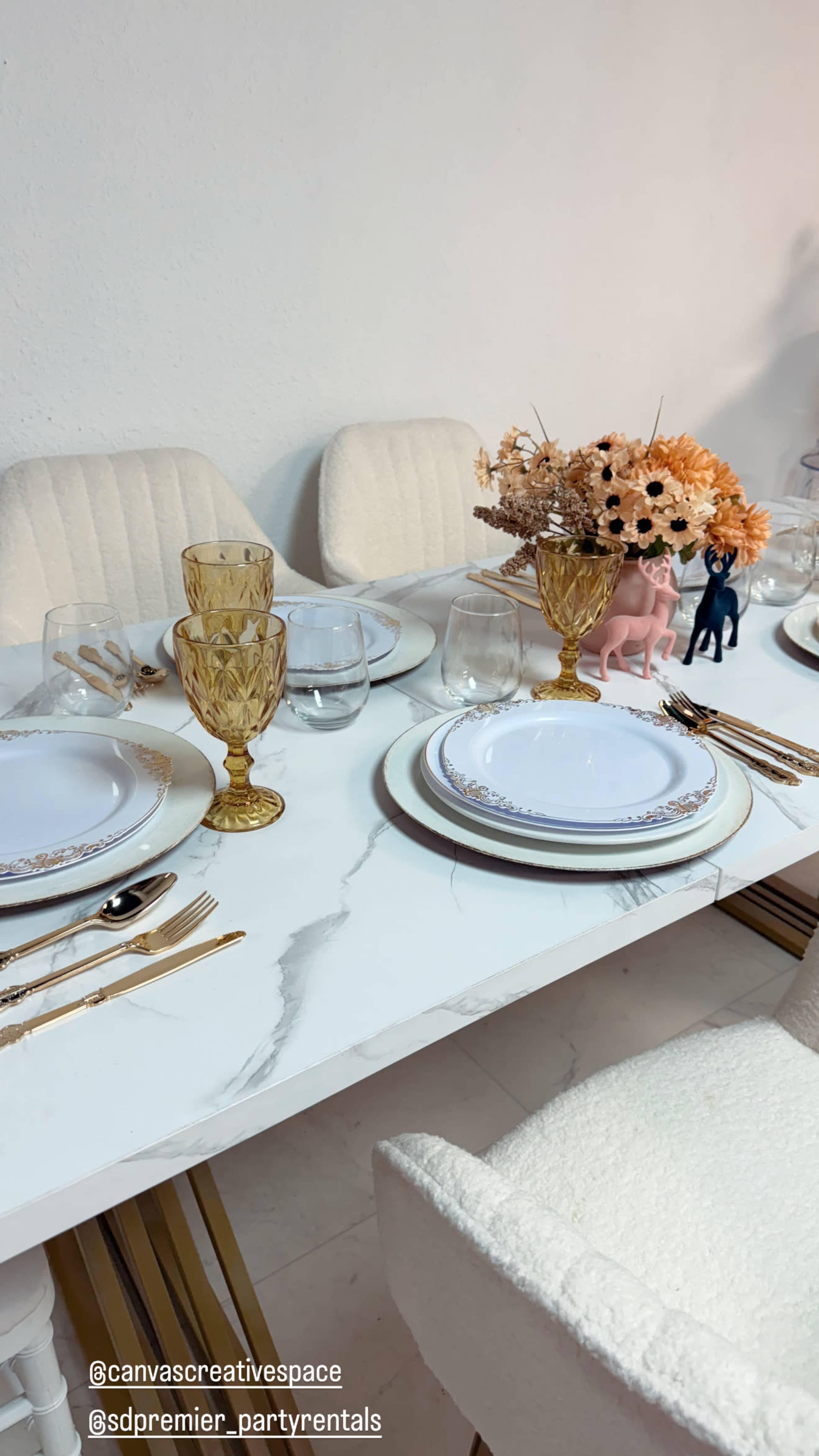 The image shows a beautifully set dining table with elegant plates, glassware, gold cutlery, and a floral centerpiece.
