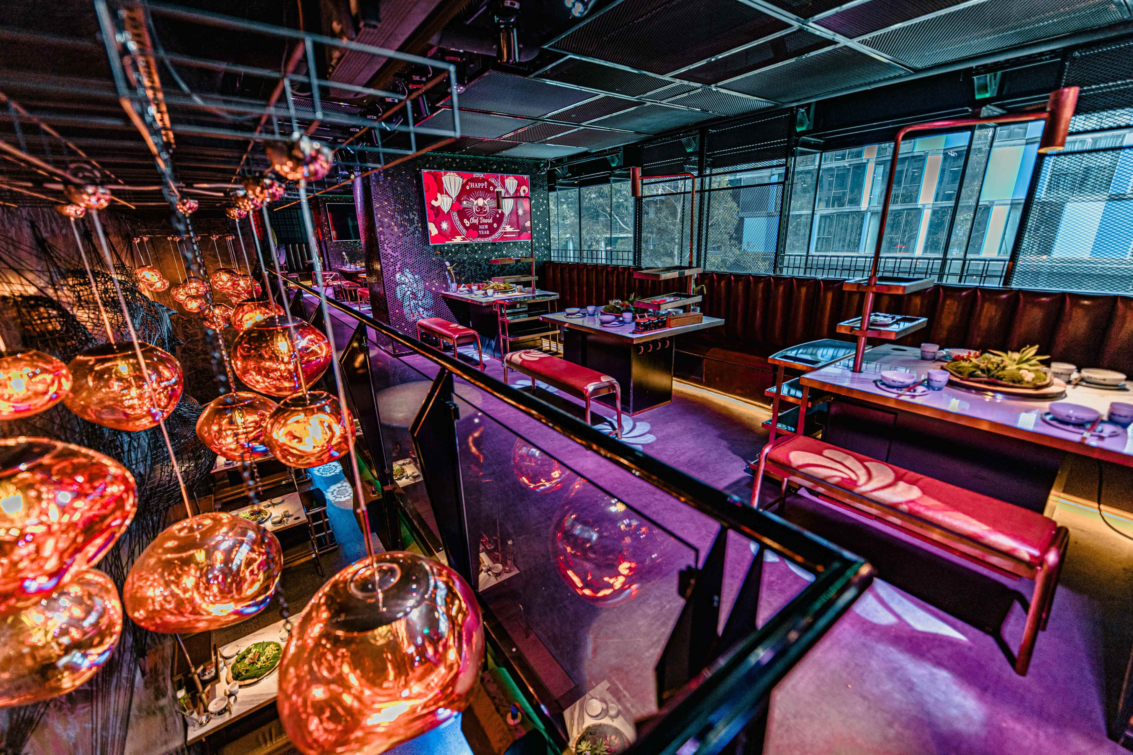 A modern restaurant interior with hanging glass light fixtures, tables set for dining, and large windows providing a city view.