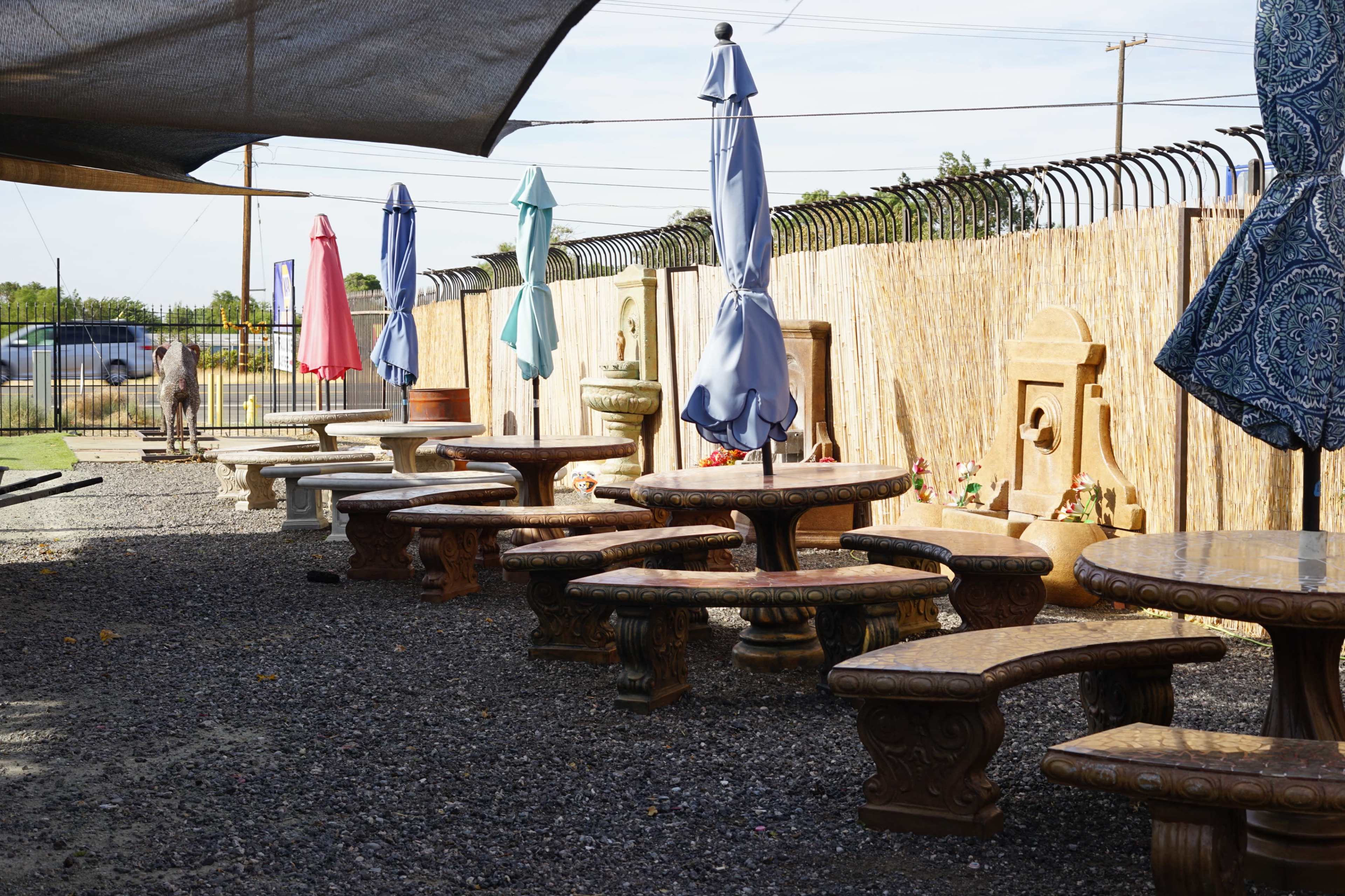 The image shows a row of stone benches arranged under shaded umbrellas beside a gravel pathway, with a decorative wall in the background.