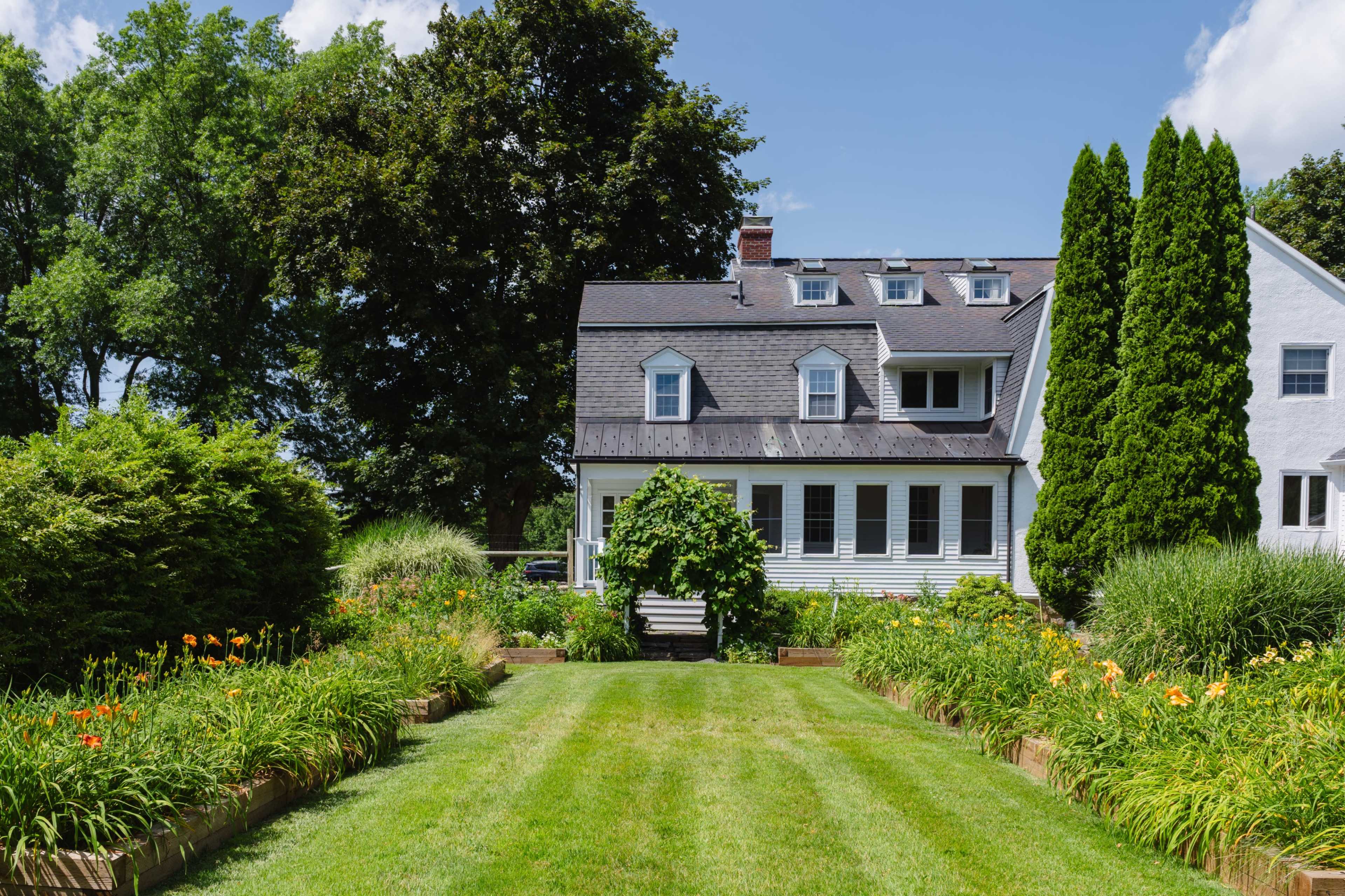 A well-maintained garden featuring colorful flower beds leads up to a large, two-story house with a gabled roof.