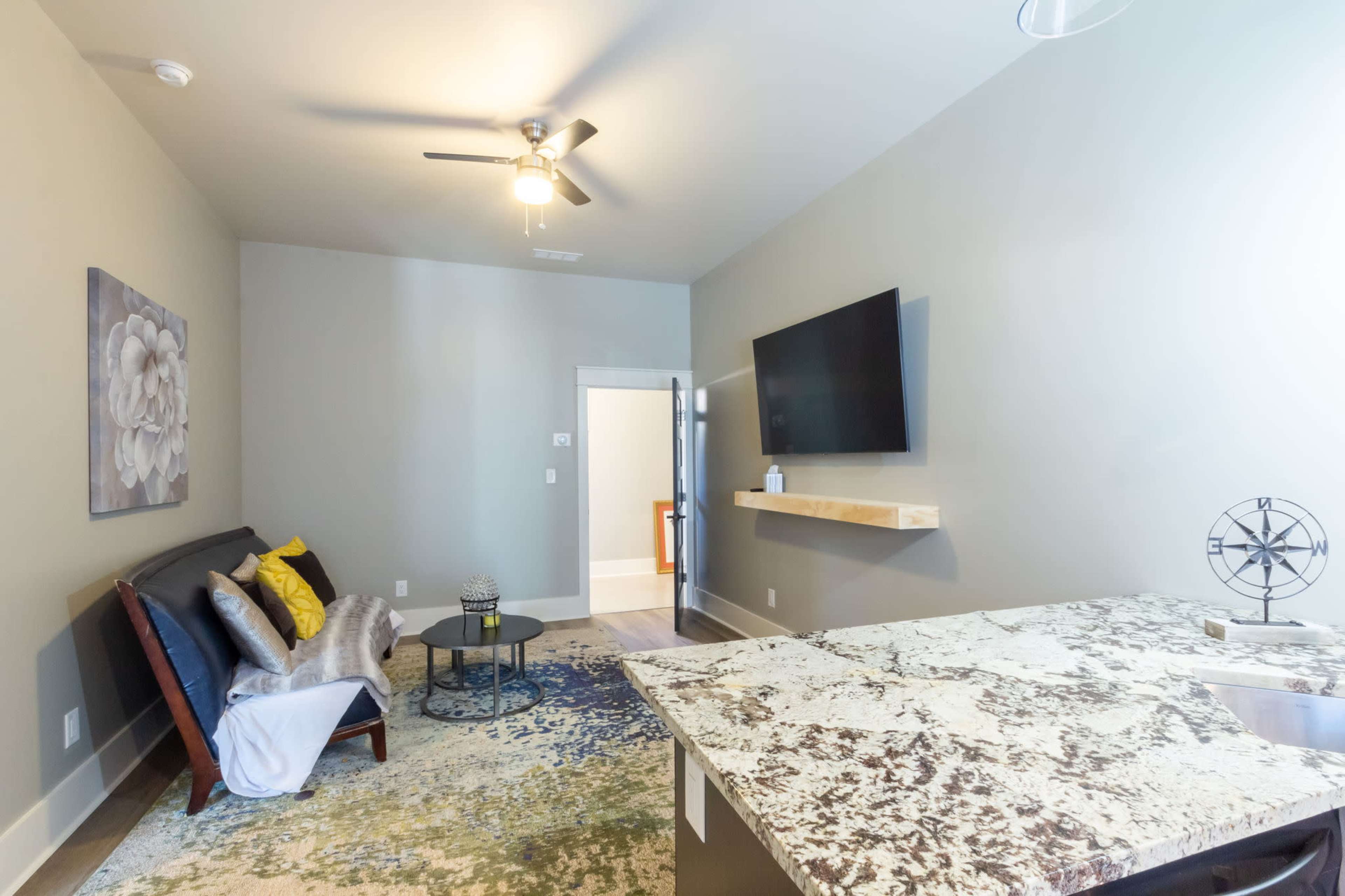 The image shows a modern living space featuring a sofa with decorative pillows, a round coffee table, a wall-mounted television, and a patterned area rug.