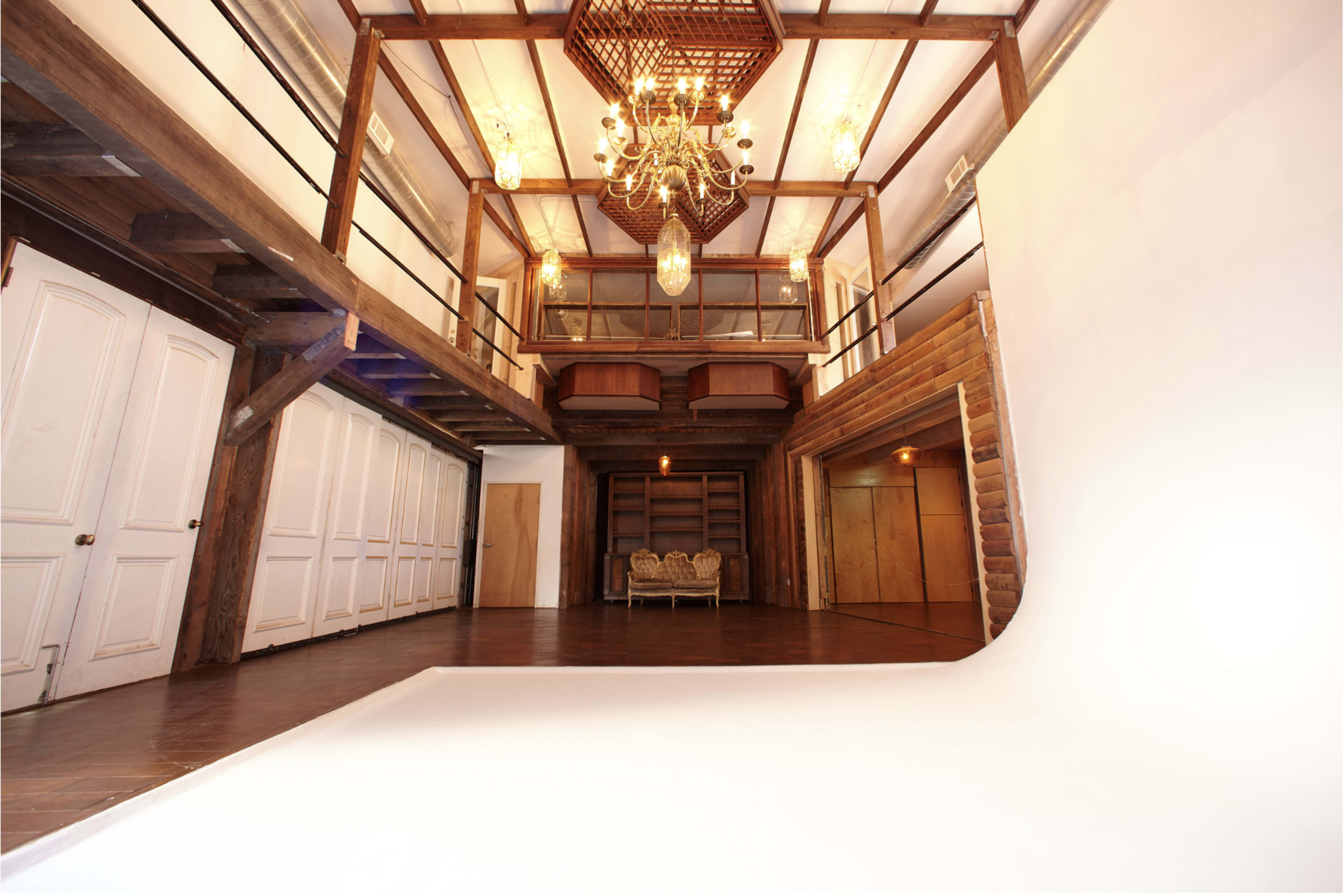 A spacious interior with high ceilings, large windows, wooden beams, and a white photography backdrop in the foreground.