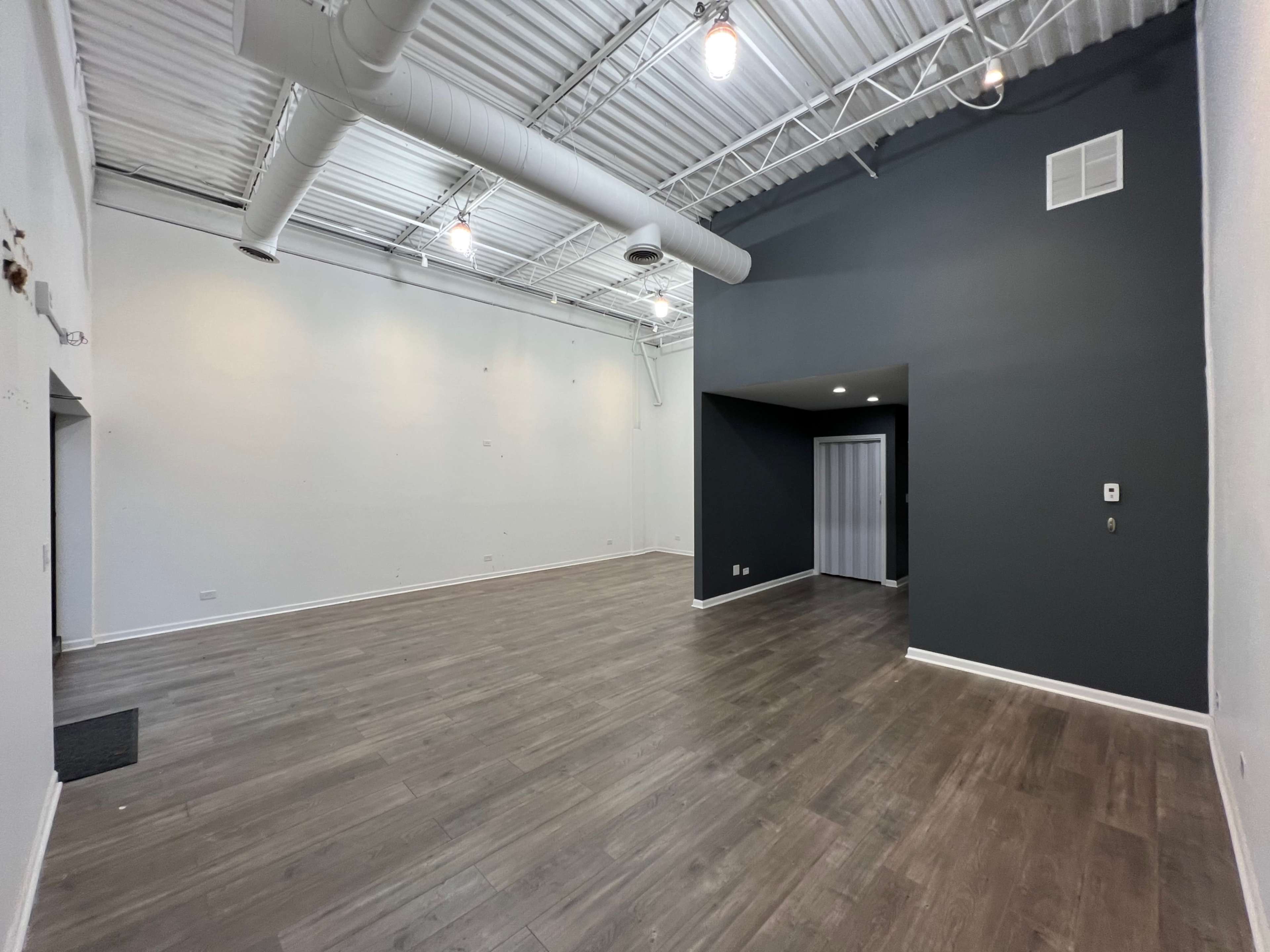 An empty room with wooden flooring, white walls, and a dark accent wall, featuring a small recessed area on the right.