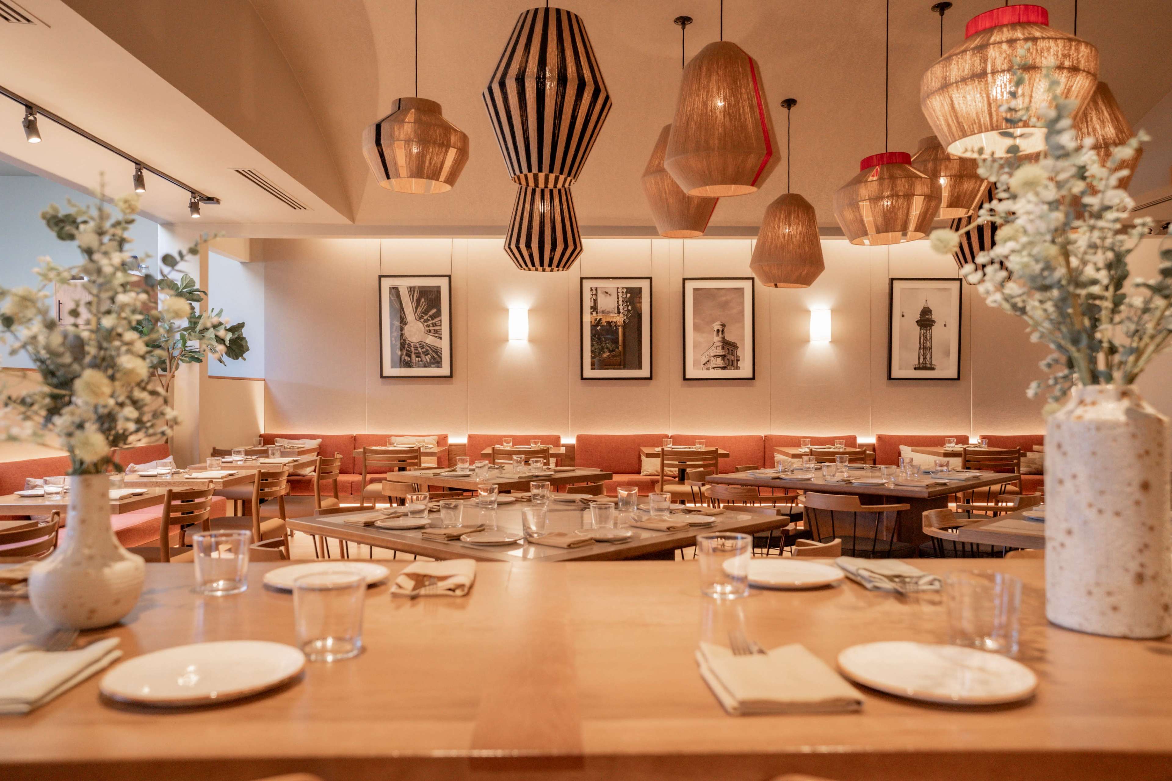 The image shows a modern restaurant interior with wooden tables, woven pendant lights, and framed black-and-white photographs on the walls.