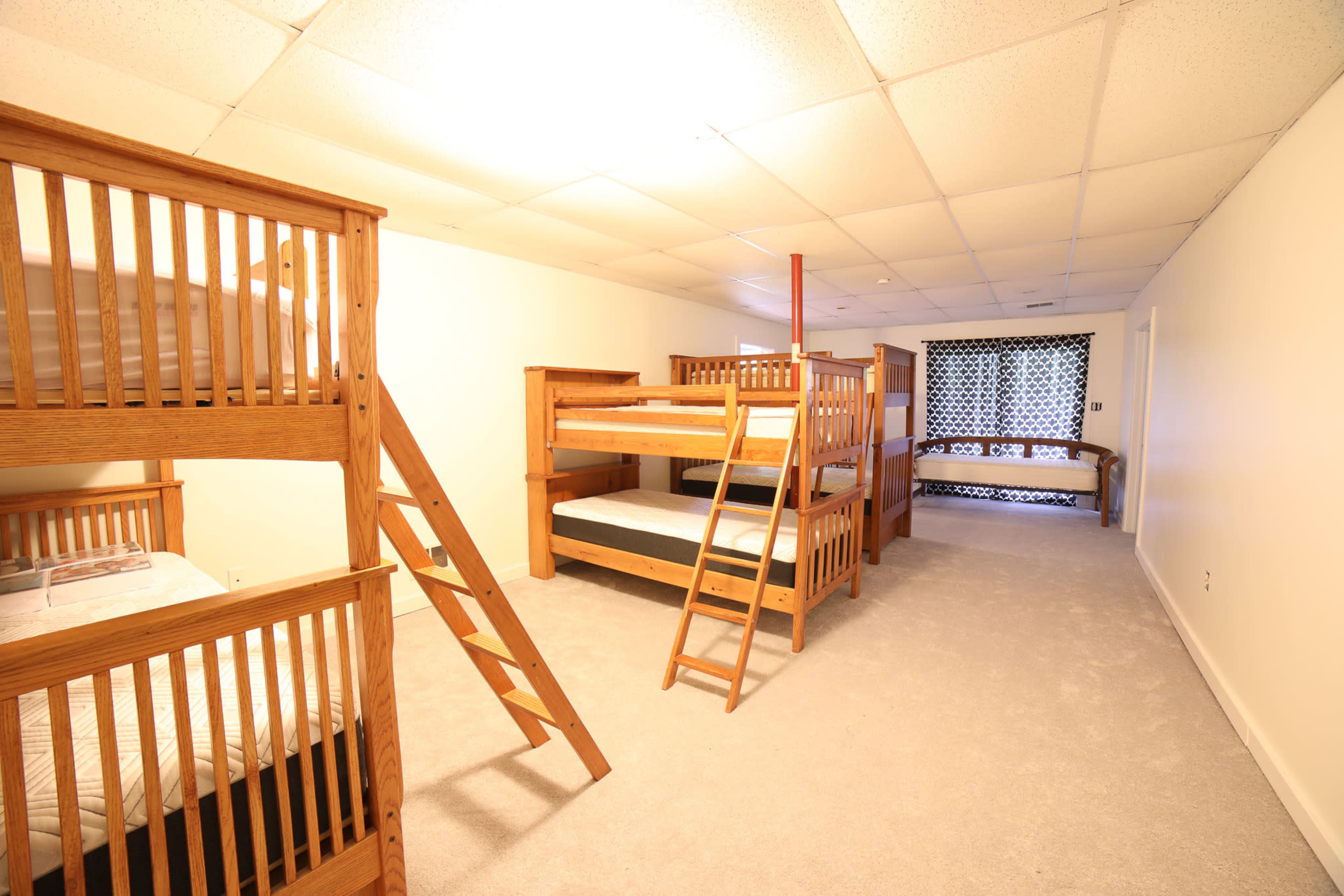 A room with two sets of wooden bunk beds and a single bed area, all arranged along a carpeted floor.