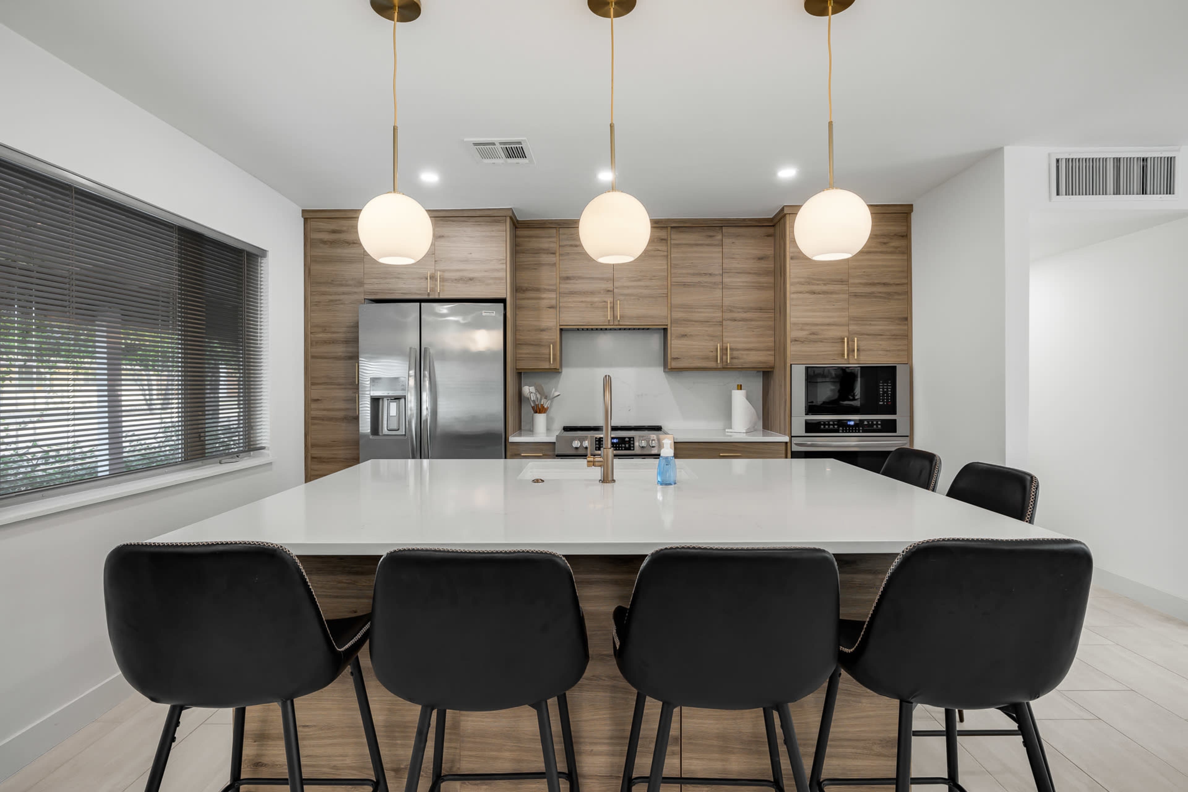 A modern kitchen with a large island, six black bar stools, and pendant lighting.