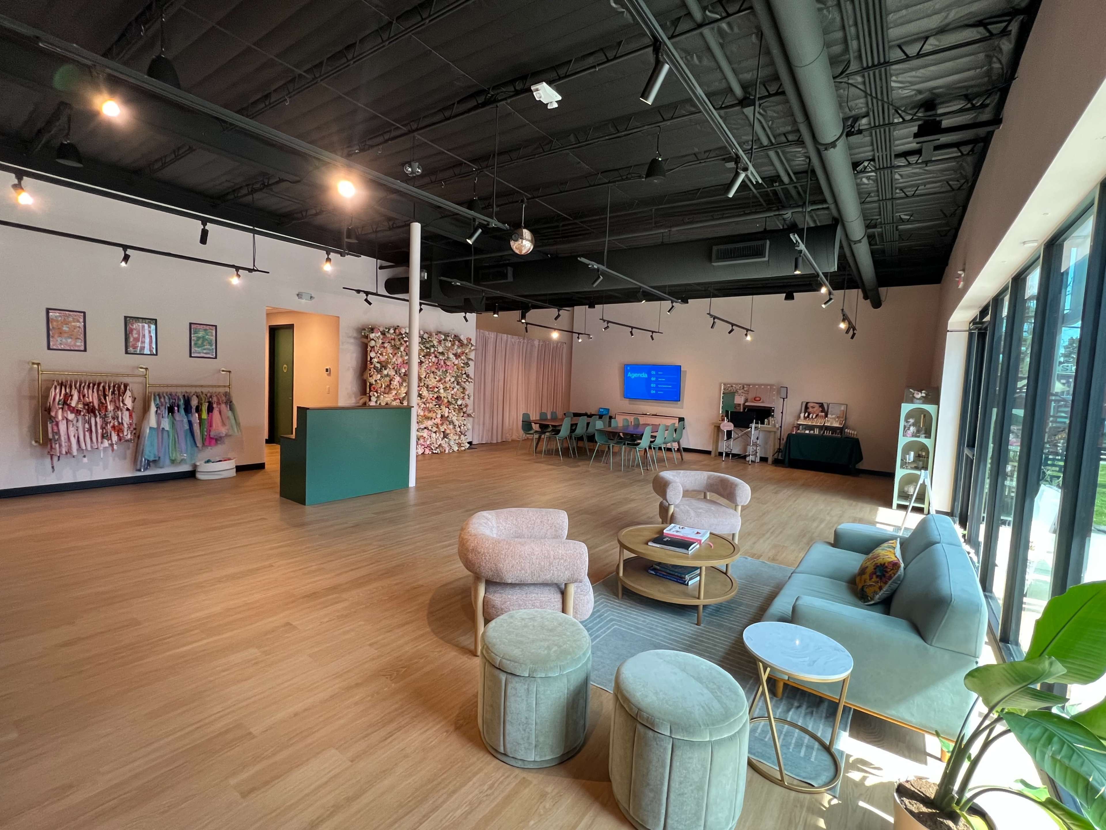 The image shows a spacious, modern interior room with seating areas, decorative elements on the walls, and a variety of colorful garments displayed on racks.