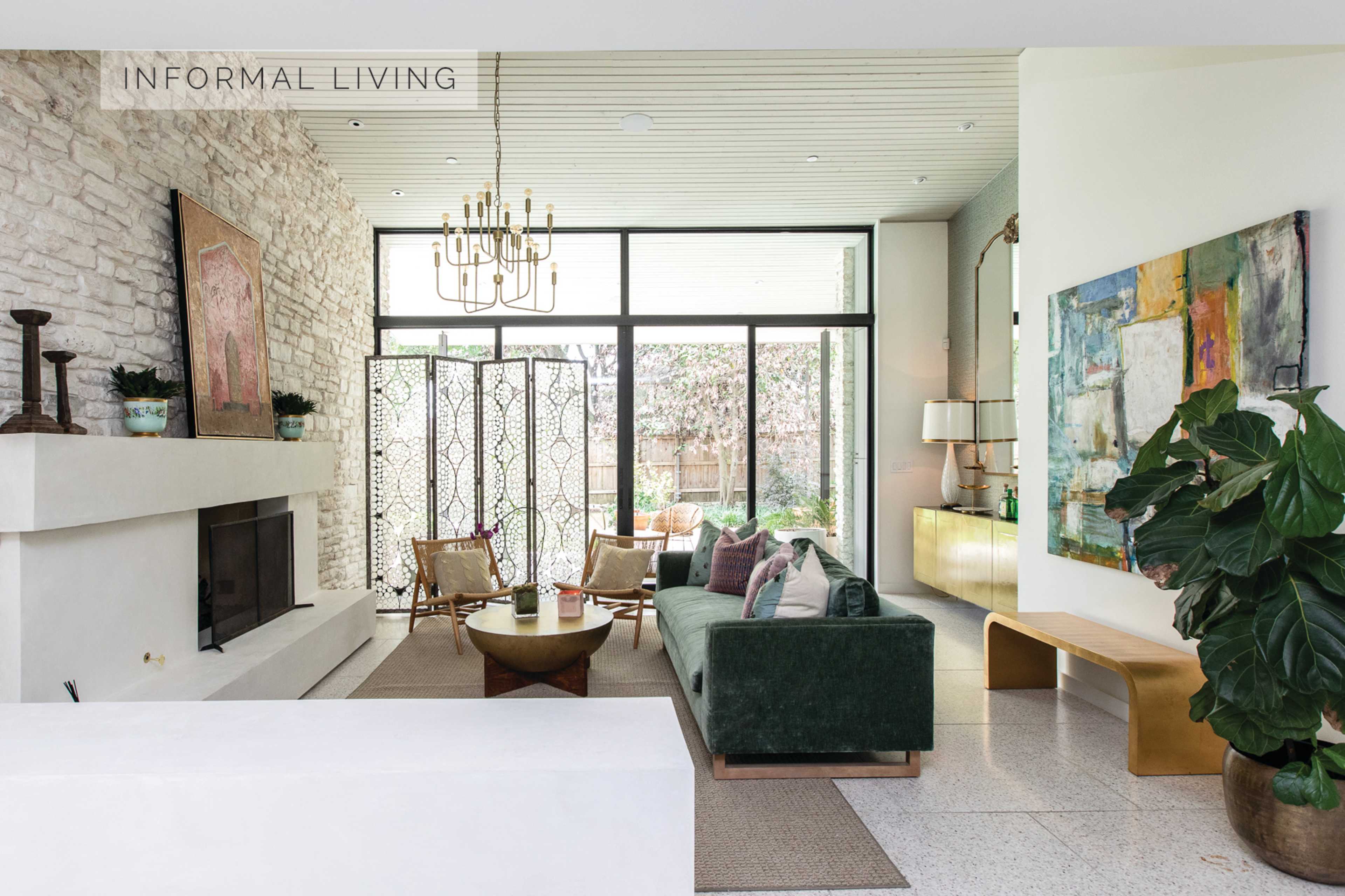 A modern living room with a green sofa, a stone fireplace, large windows, and a mix of stylish furniture elements.