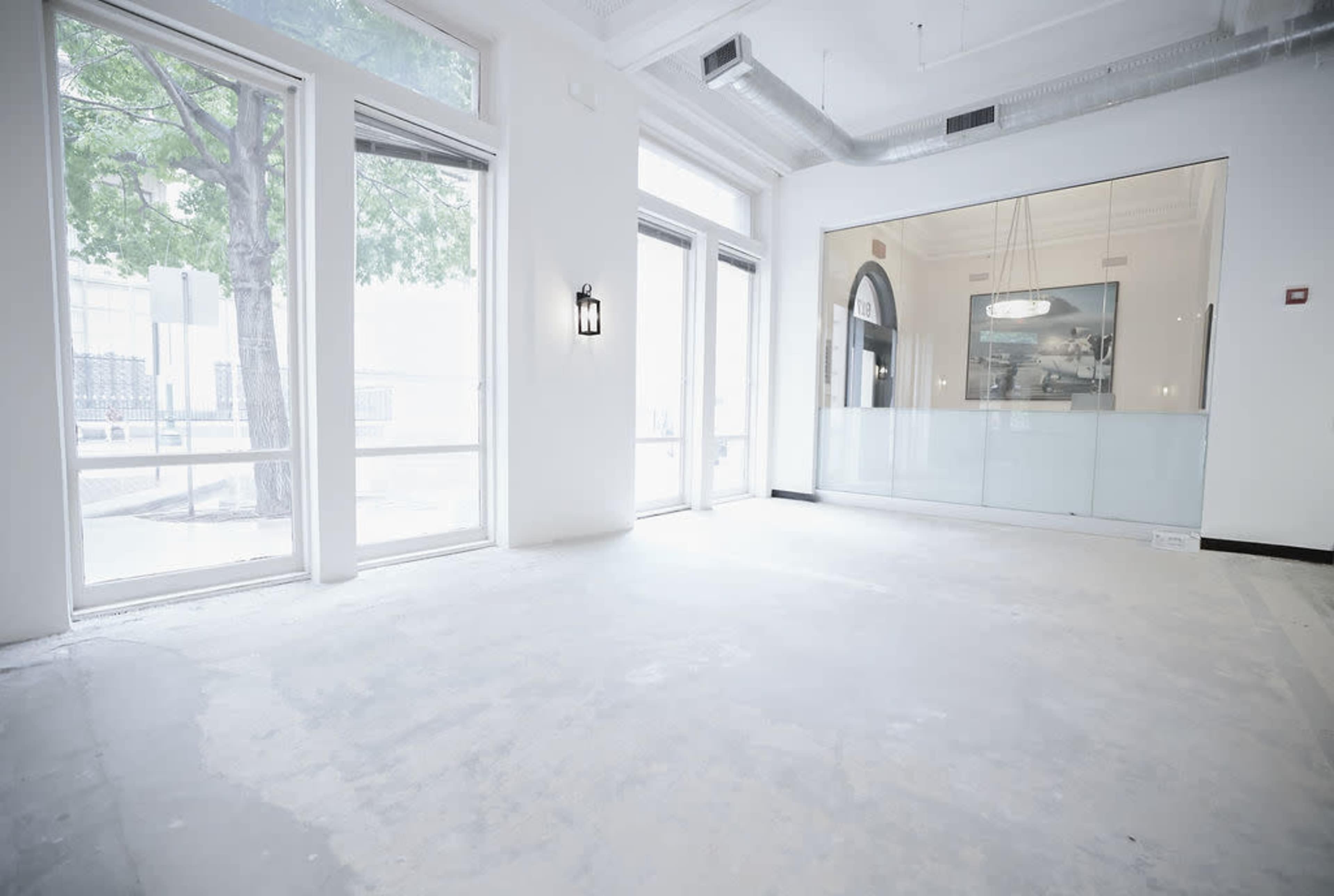 The image shows an empty room with large windows, a glass partition, and unfinished flooring.