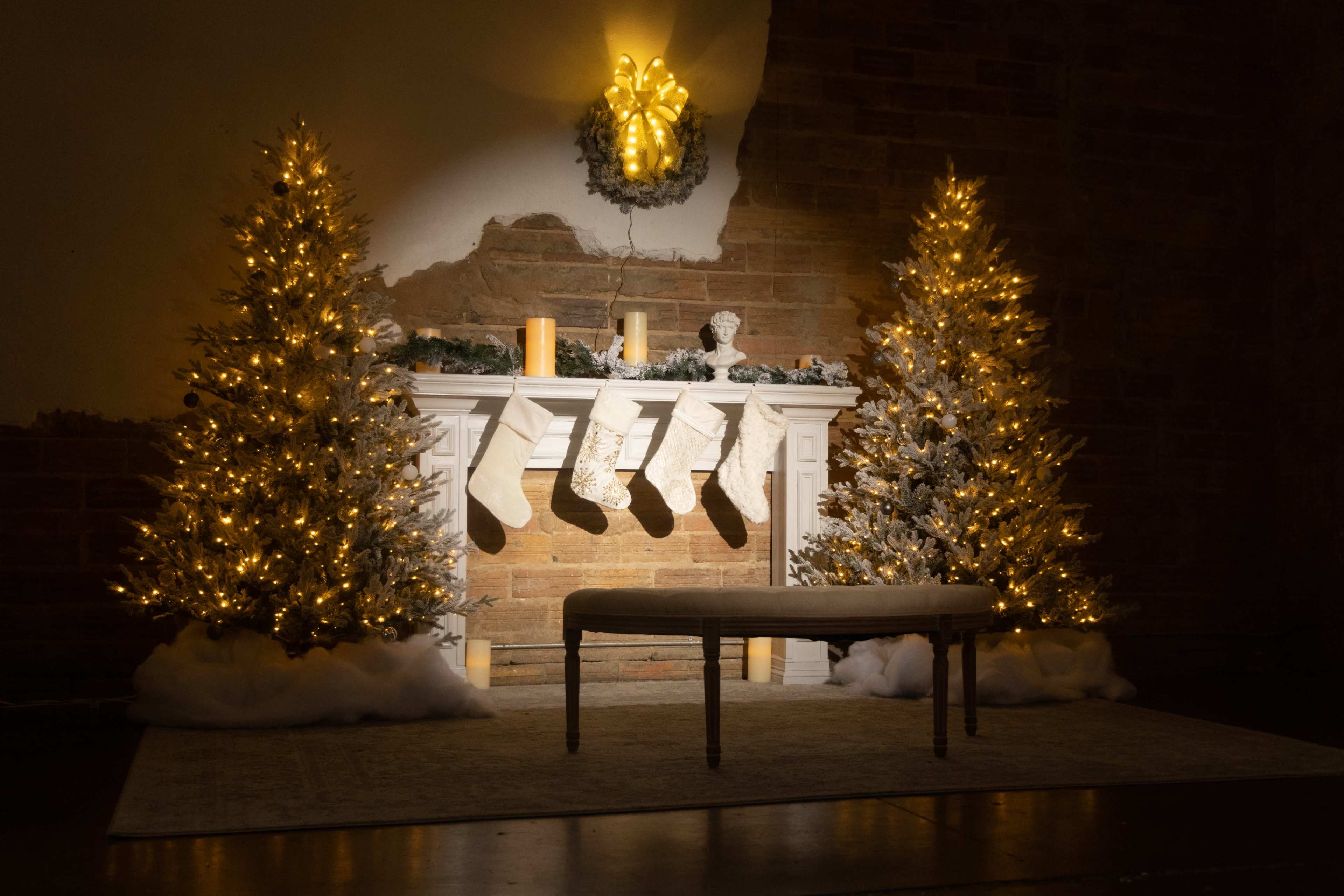 The scene features a decorated fireplace with two illuminated Christmas trees, stockings hung above, and a bench in front.