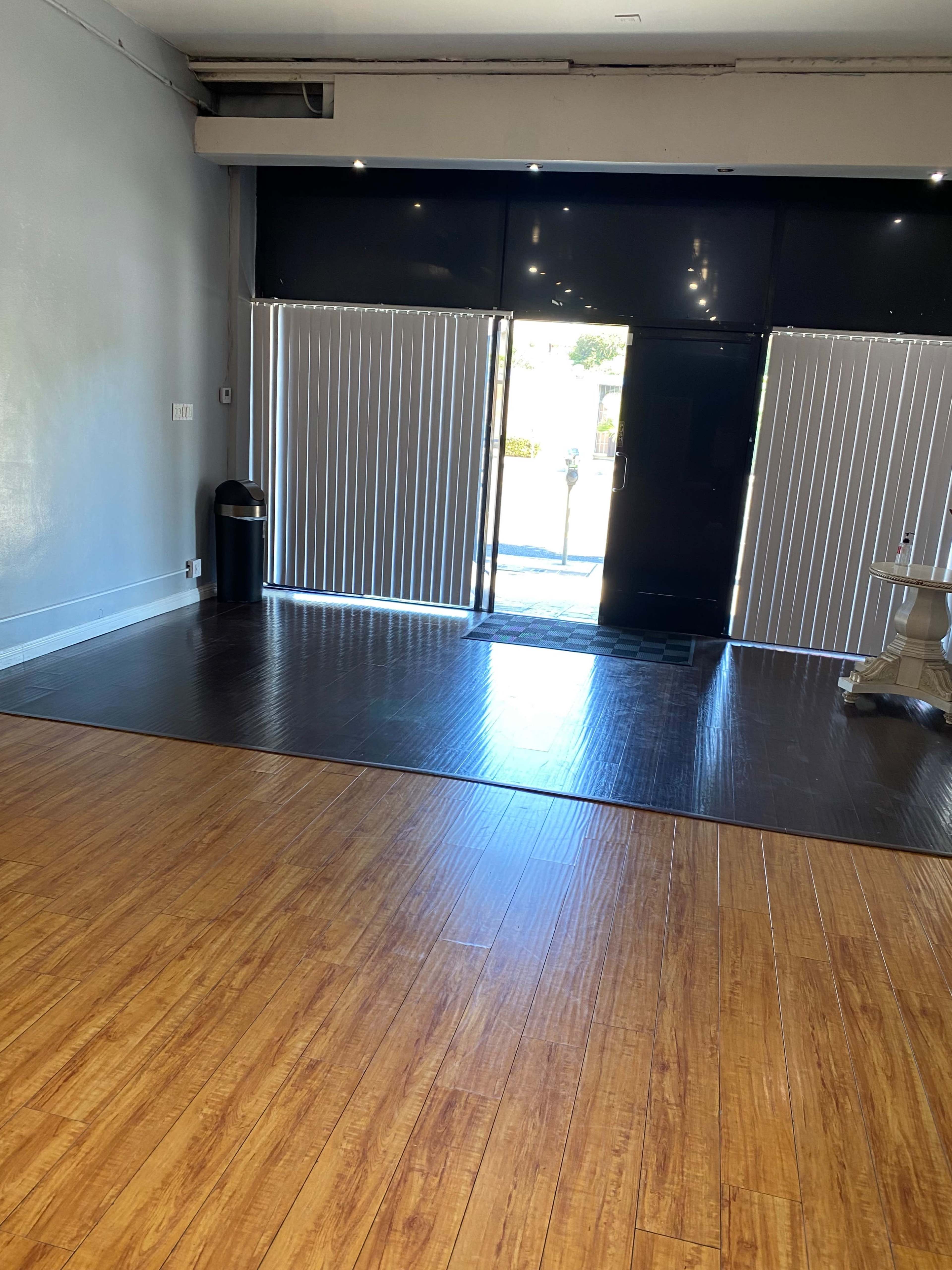 The image shows an empty interior space with a wooden floor and large glass doors that lead outside.