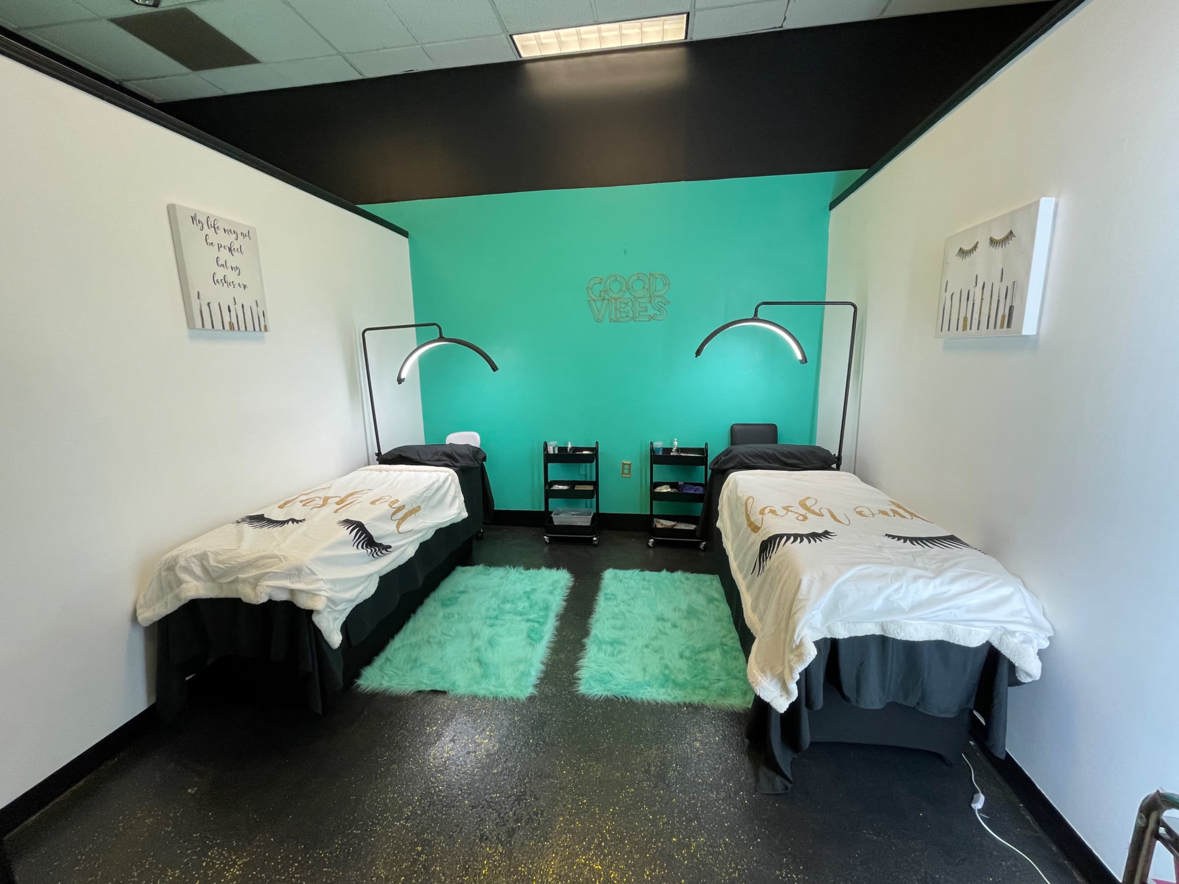 A room with two neatly made beds, green rugs on the floor, and modern light fixtures on either side.