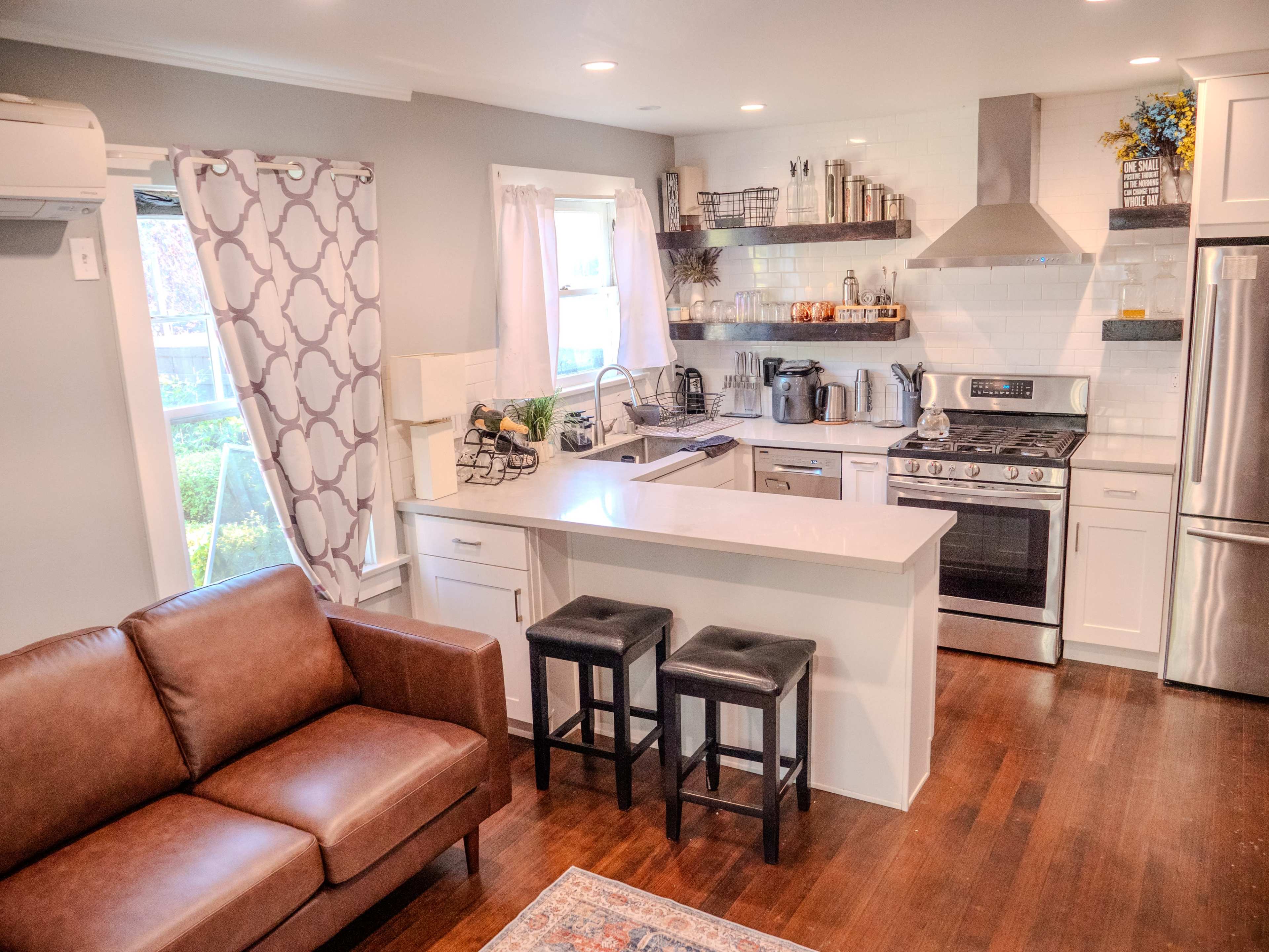 A modern kitchen with a countertop island, stainless steel appliances, a gas stove, and a brown leather couch in the living area.