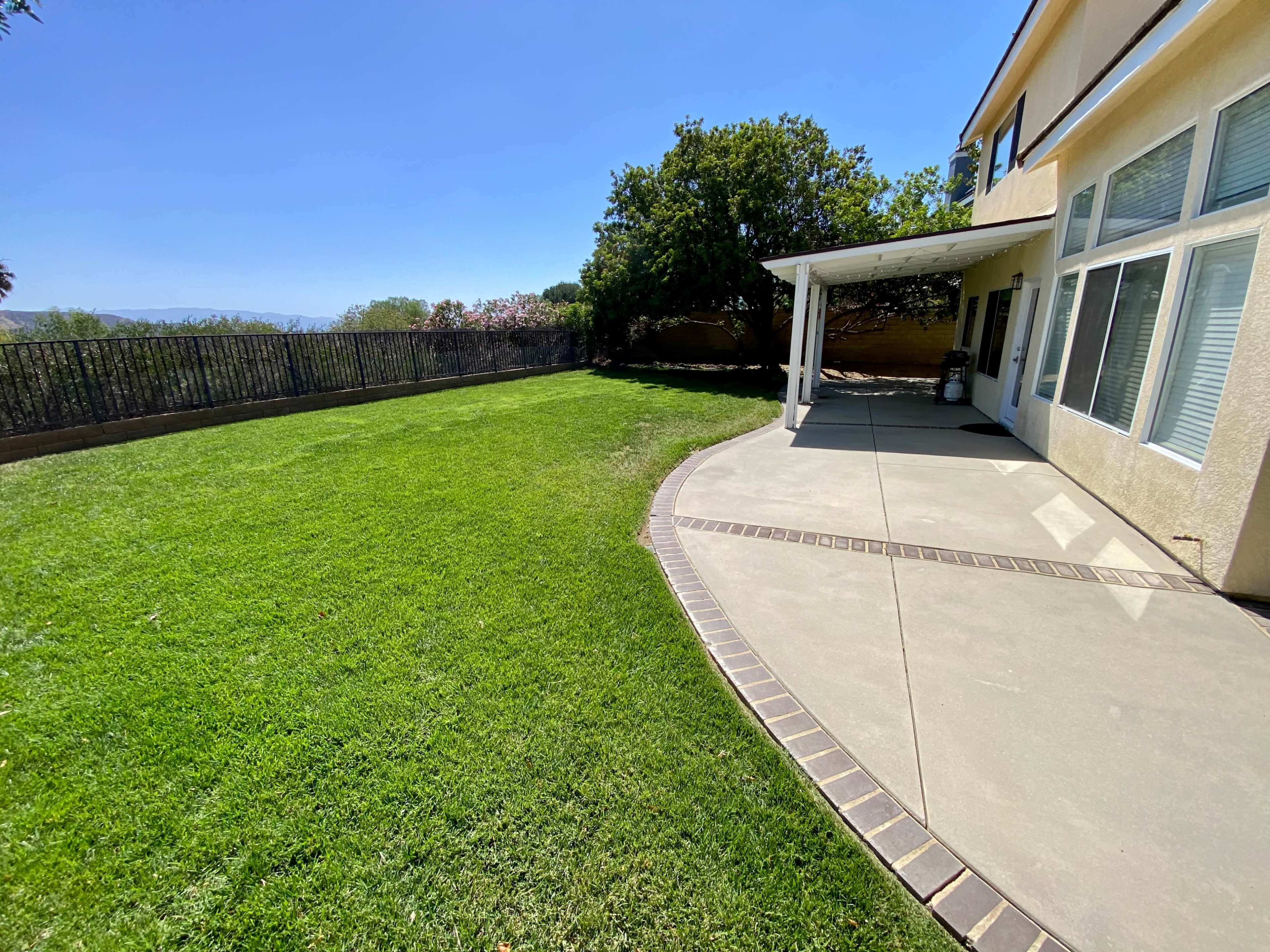 A spacious backyard features a well-manicured lawn and a concrete patio adjacent to a two-story house.