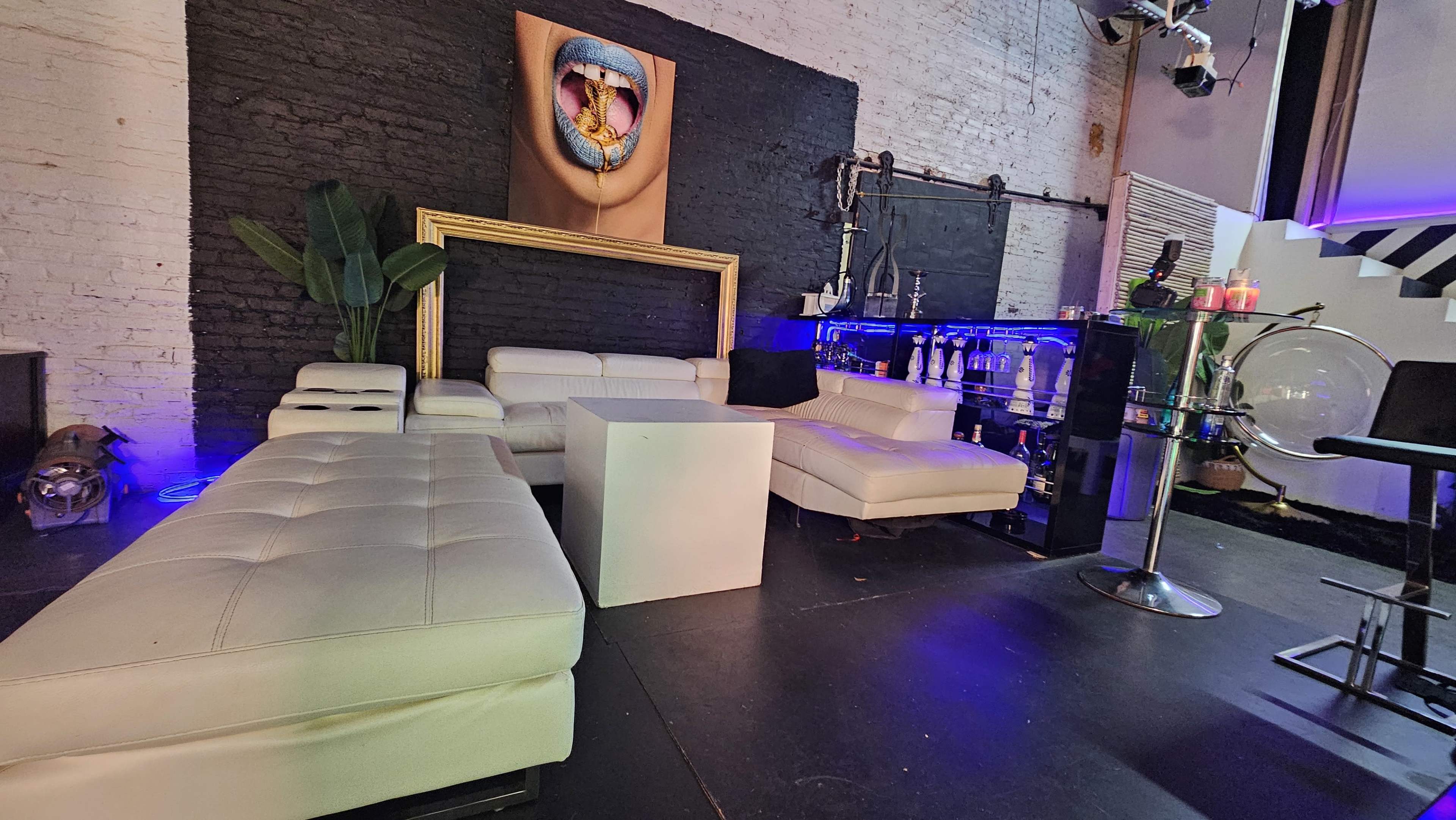 A modern lounge area featuring white leather furniture, a bar with various bottles, and a large artwork hanging on the wall.