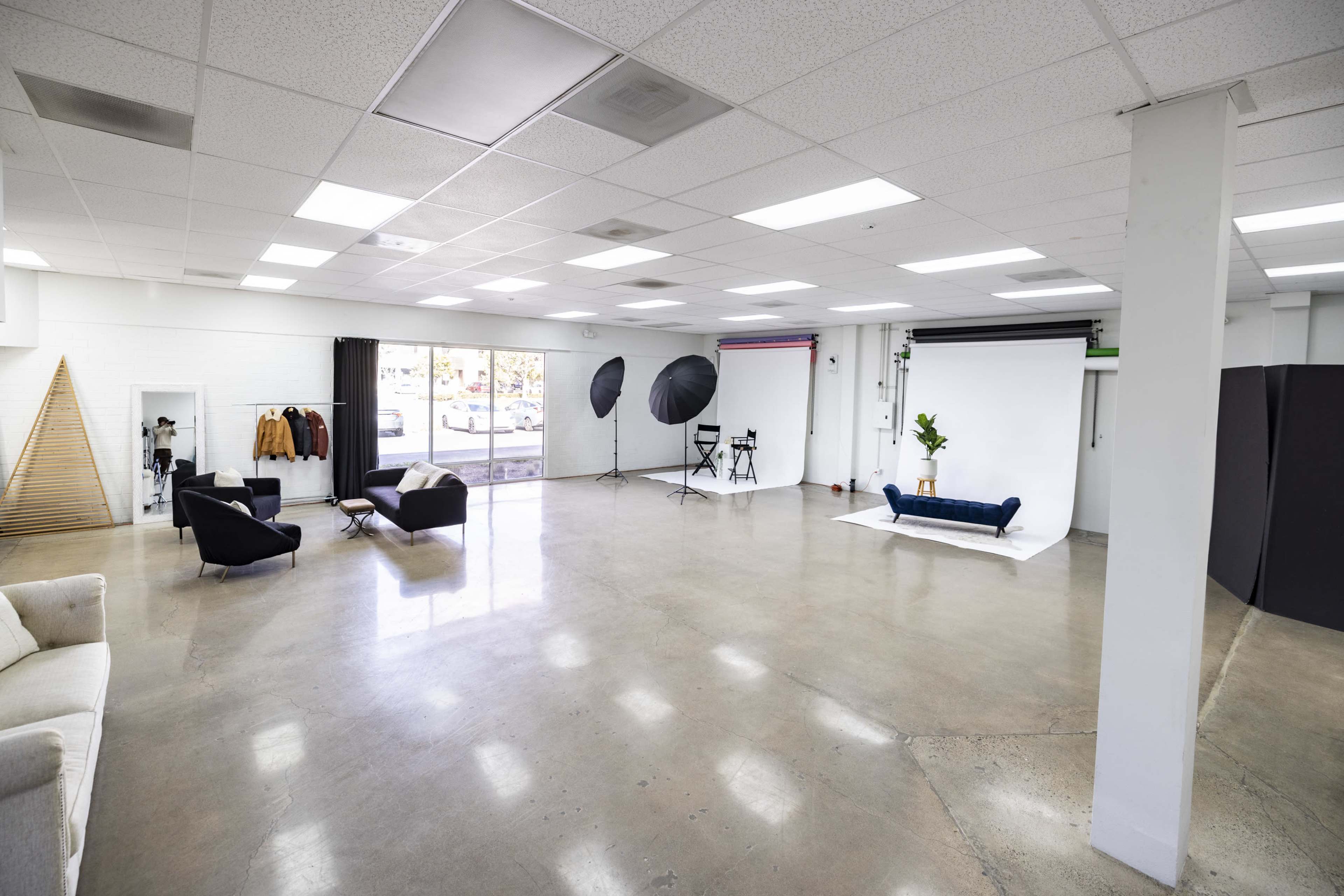 A spacious photography studio with polished concrete floors, seating areas, and lighting equipment set up near a white backdrop.