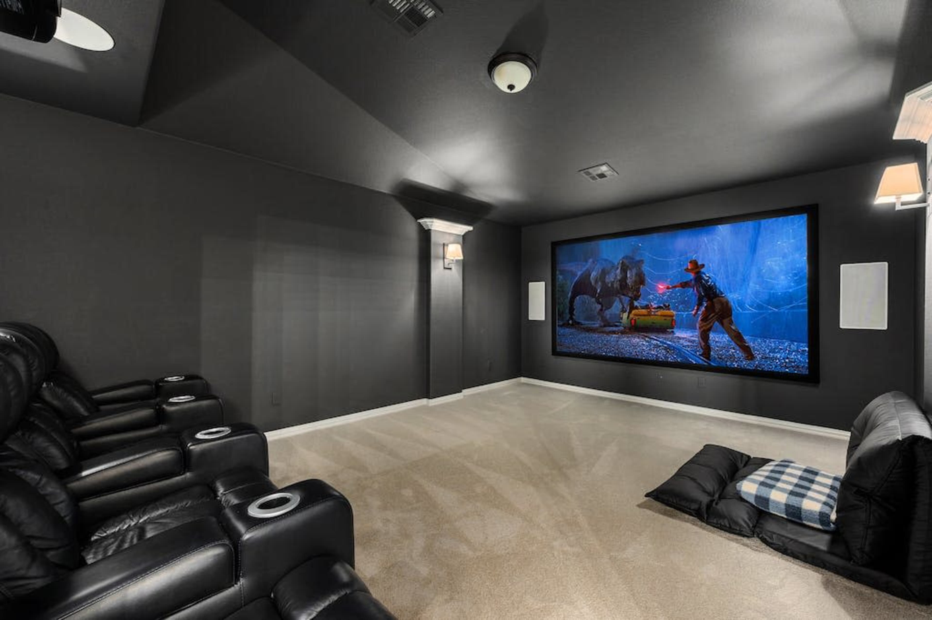 A home theater room featuring black reclining chairs, carpeted flooring, and a large projection screen displaying a scene of a cowboy confronting a bear.
