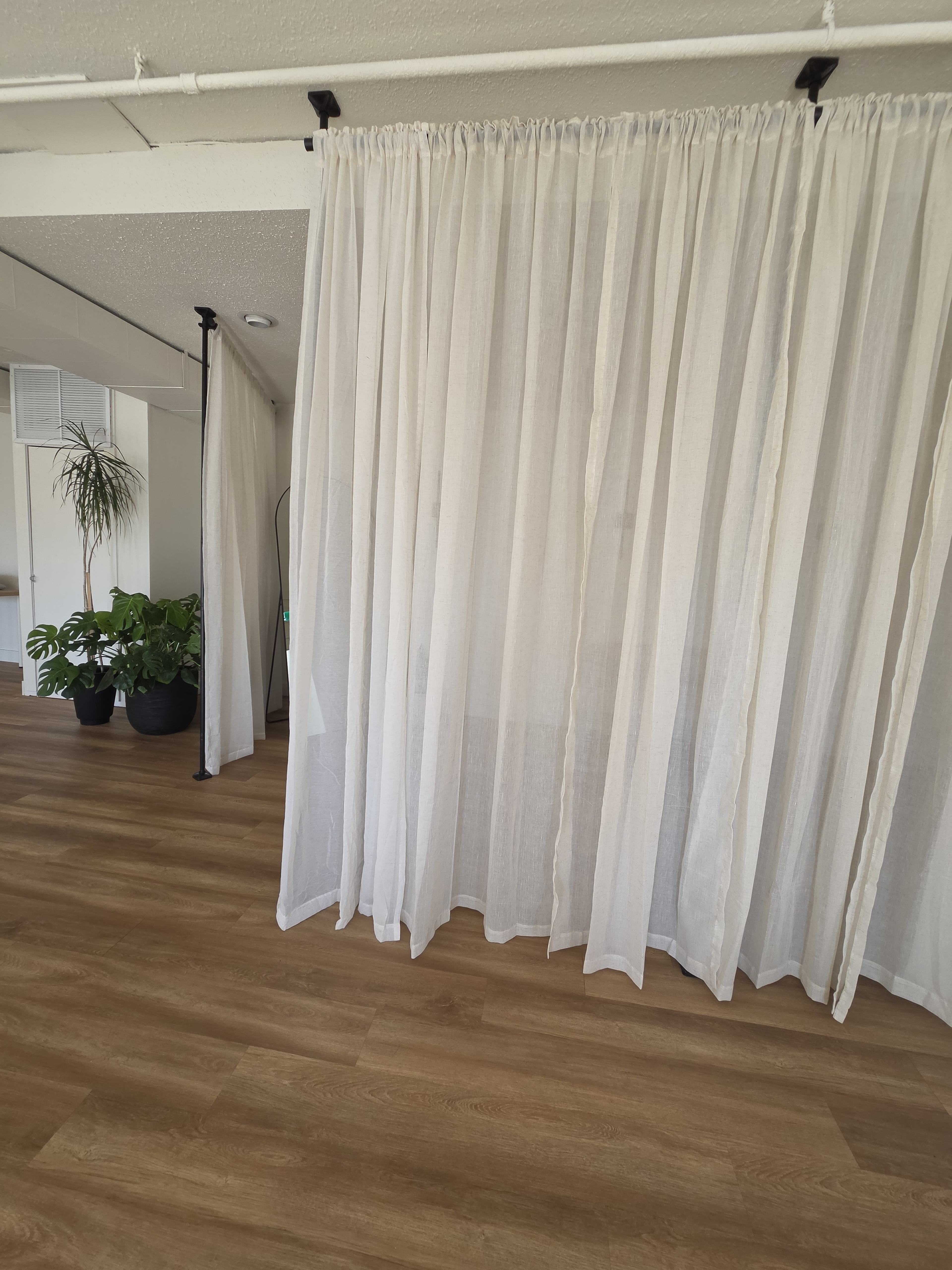 The image shows a room with light-colored sheer curtains hanging from the ceiling and potted plants visible in the background.