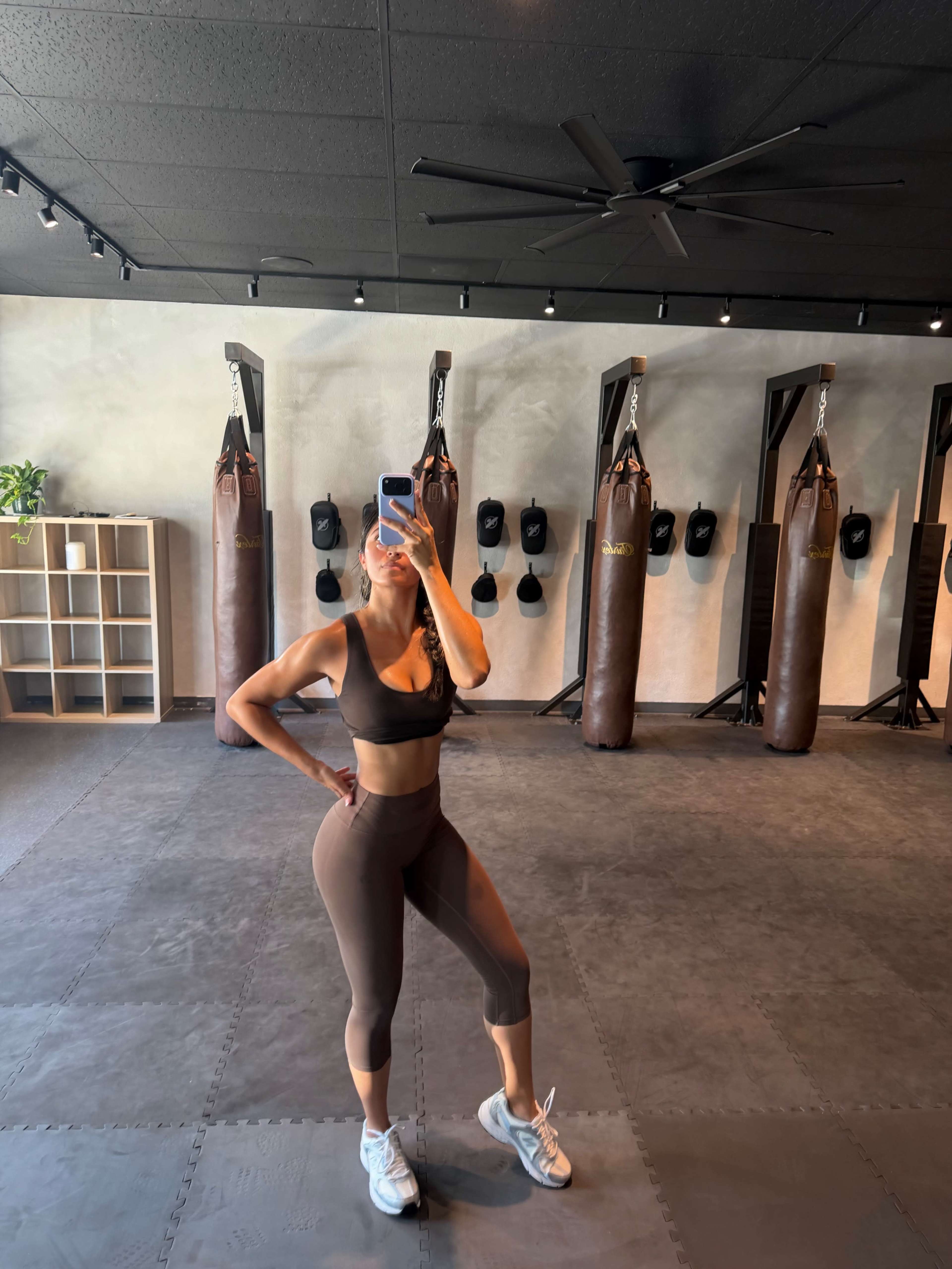 A person poses for a photo in a fitness studio equipped with punching bags and a rubber mat.
