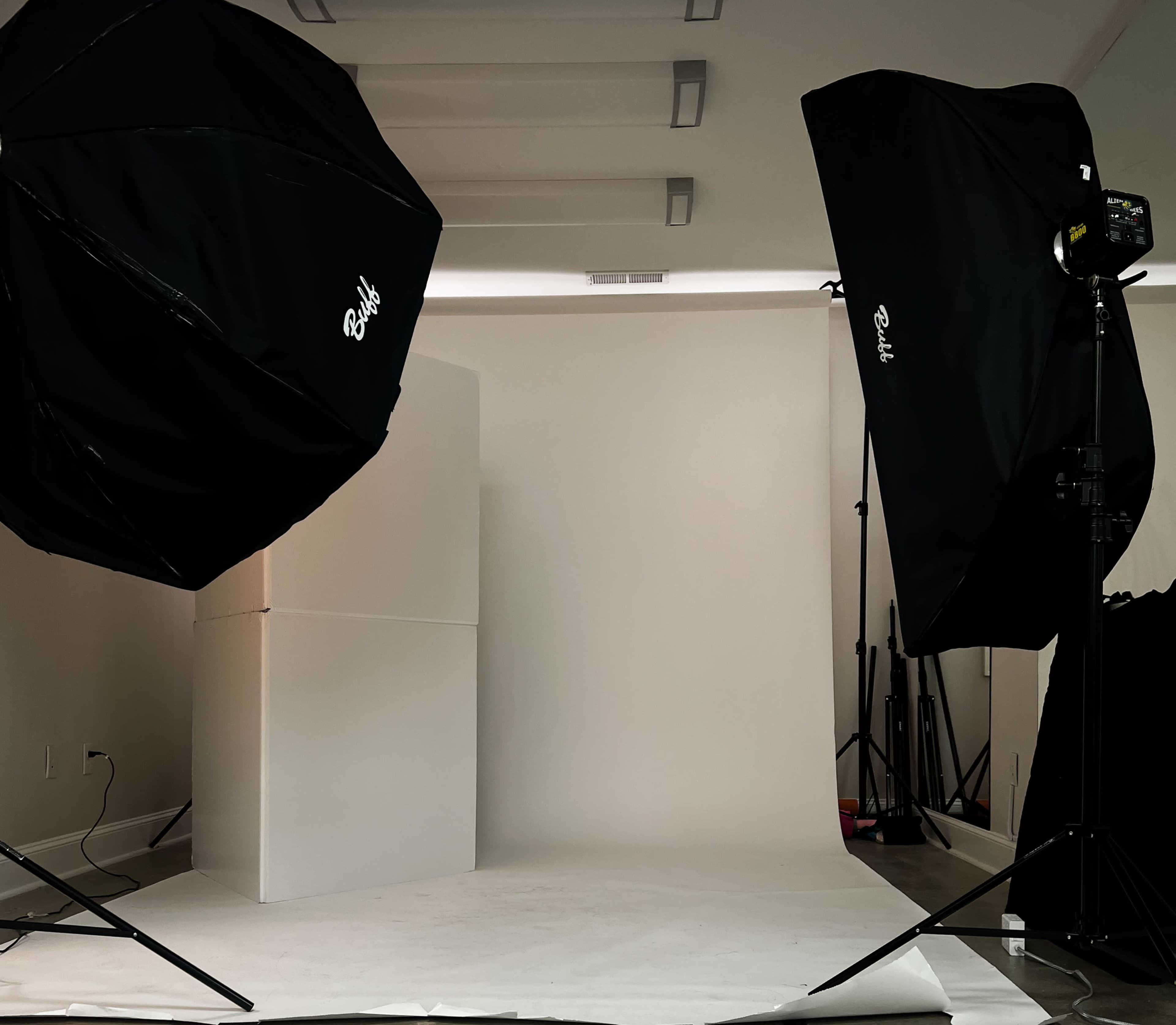 A photography studio setup features two large softbox lights directed at a blank backdrop with a white pedestal.