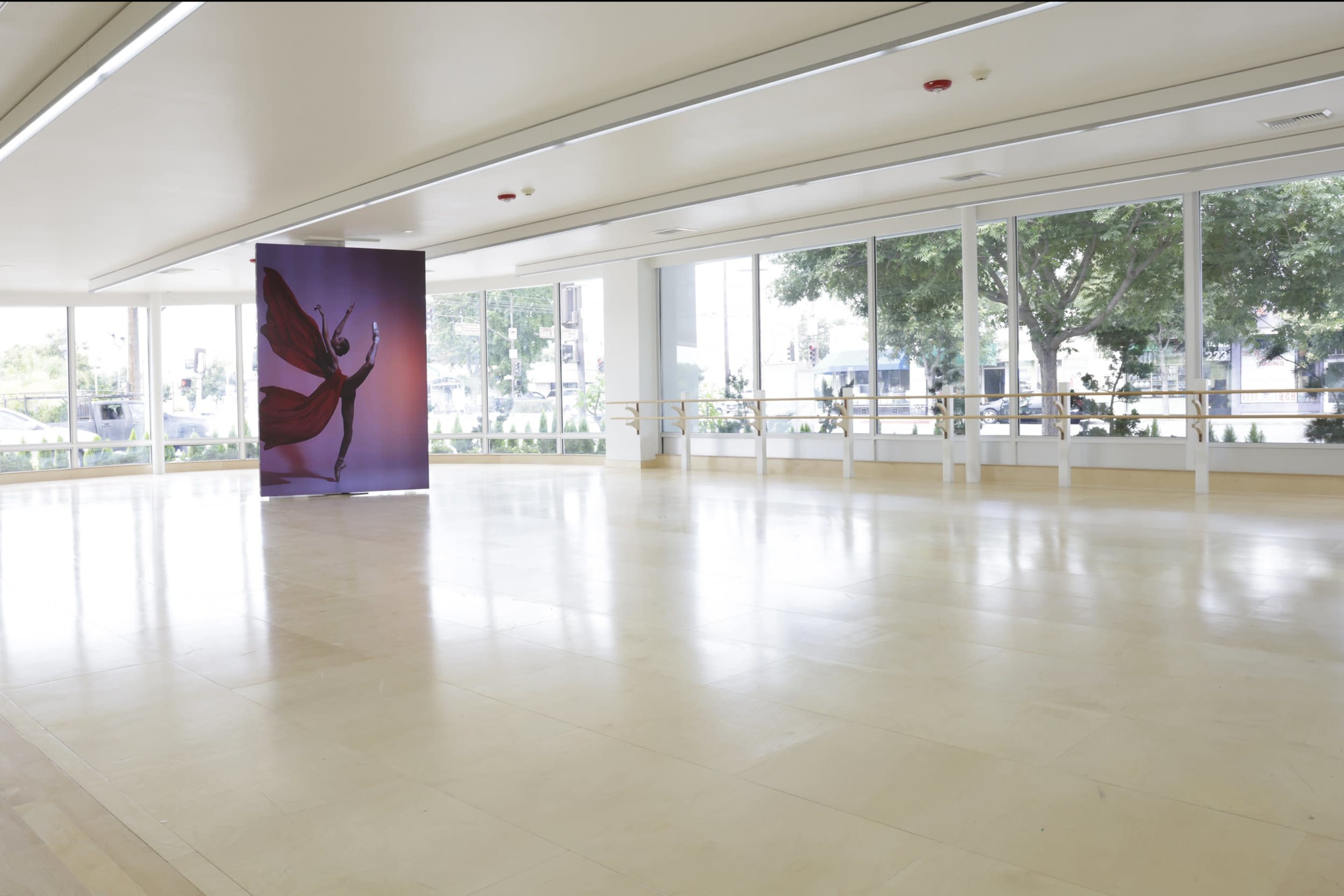 The image shows a spacious dance studio with large windows and a backdrop featuring a dancer in a flowing red costume.