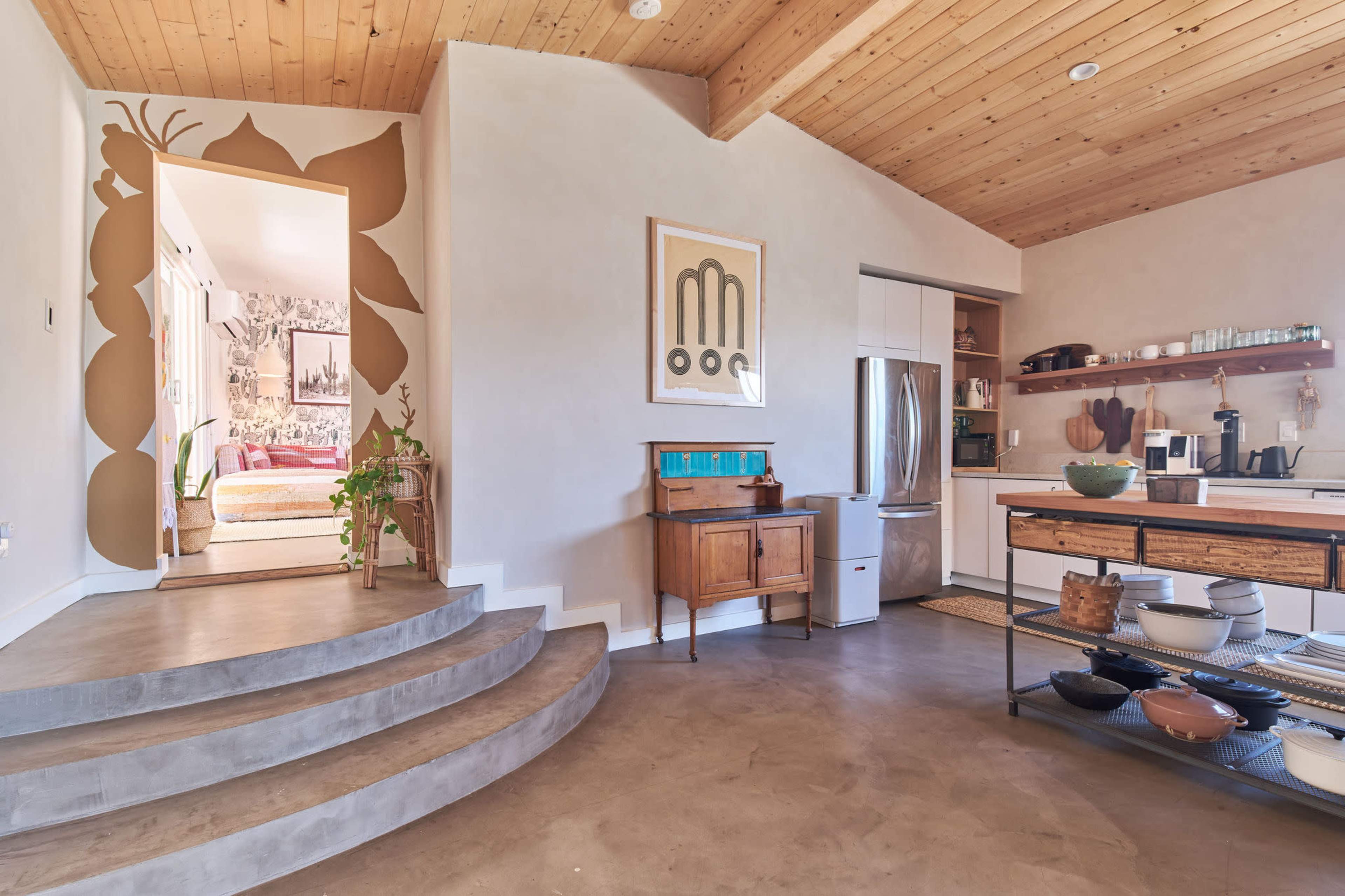 A modern interior space featuring a staircase leading to a cozy area, with a kitchen equipped with various appliances and a wooden table displaying cookware.