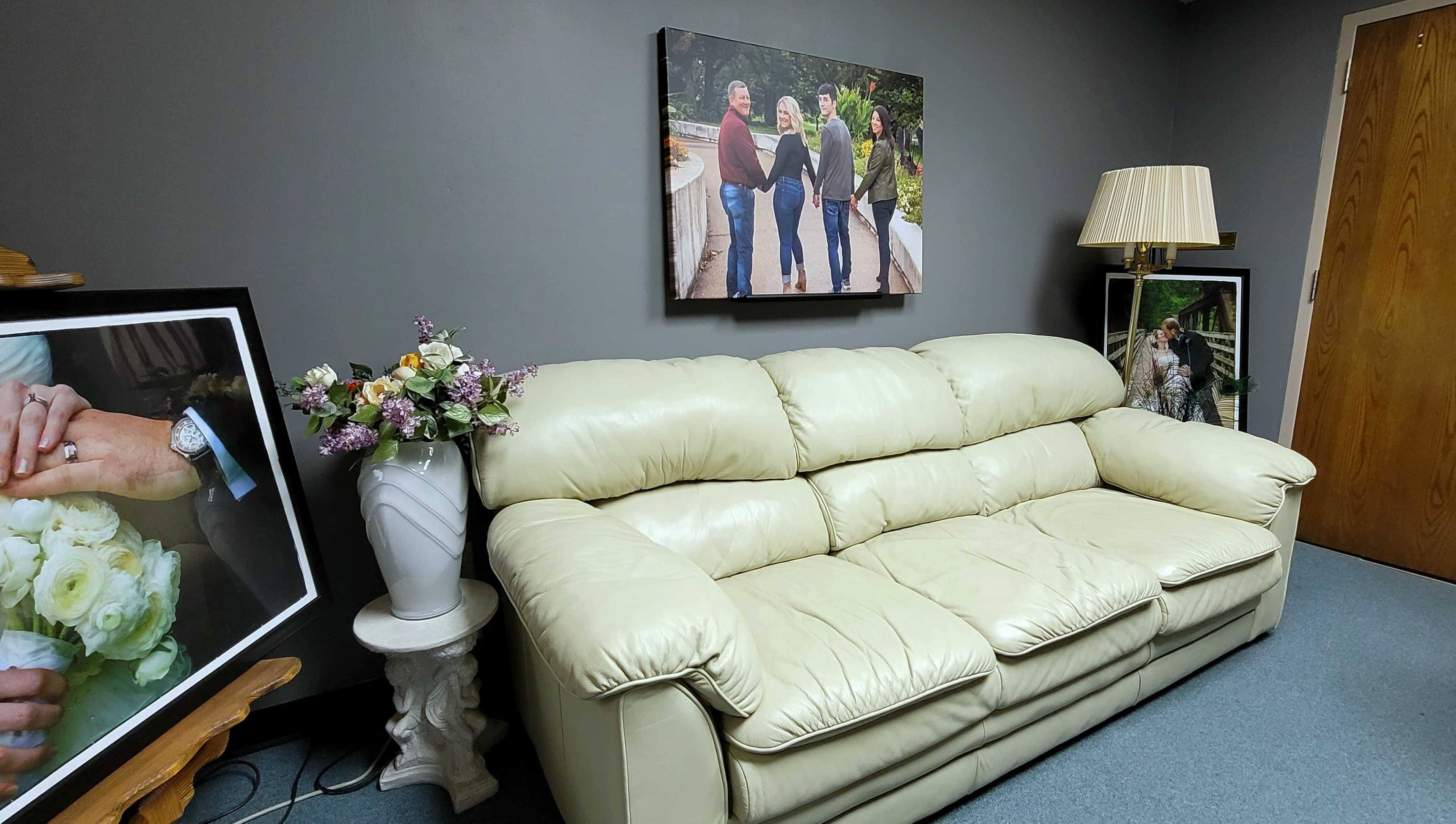 The image shows a light-colored couch situated in a room decorated with framed photographs and a vase of flowers.