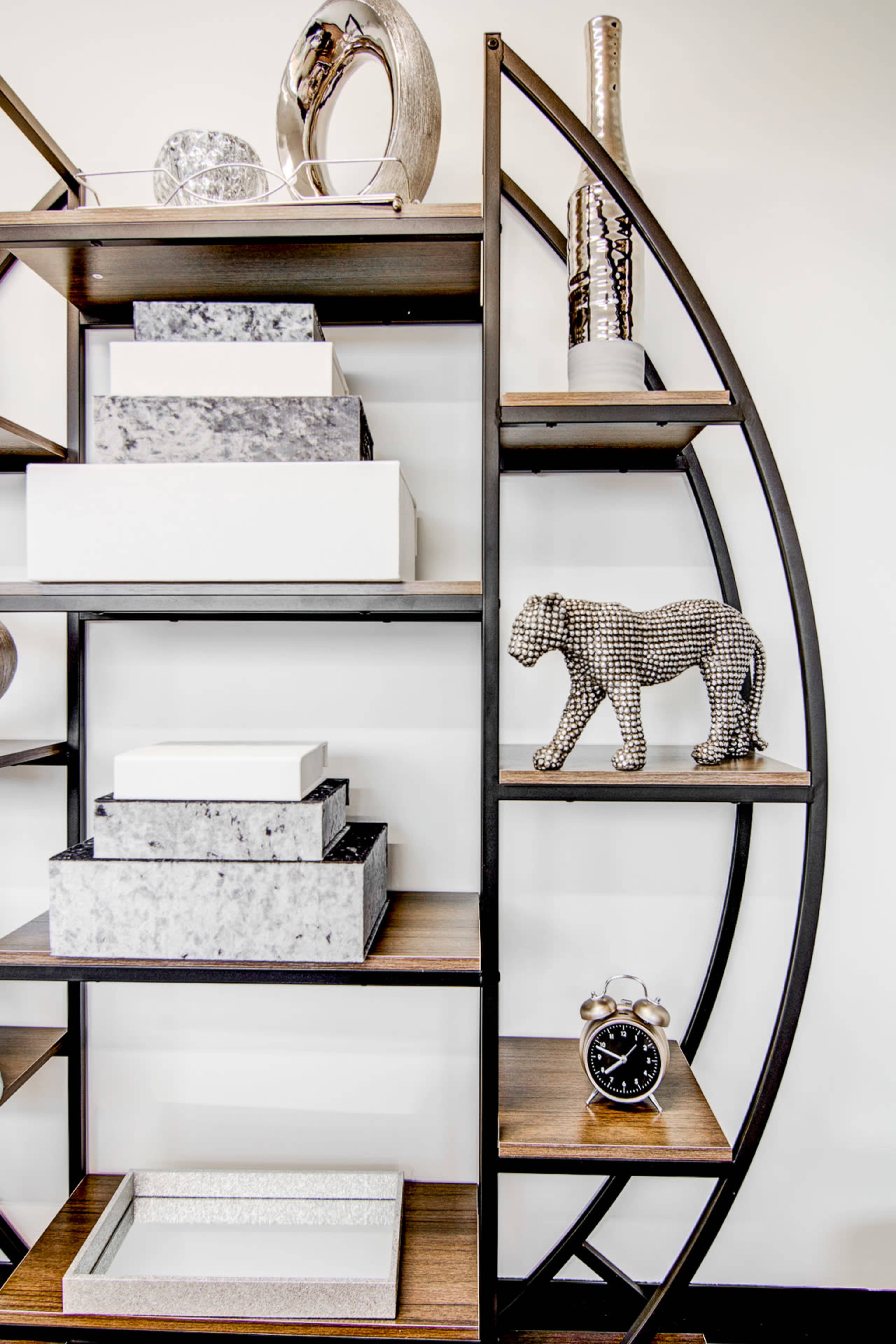A modern bookshelf with a circular design, showcasing various decorative items, including boxes, a statue of a lion, and a clock.