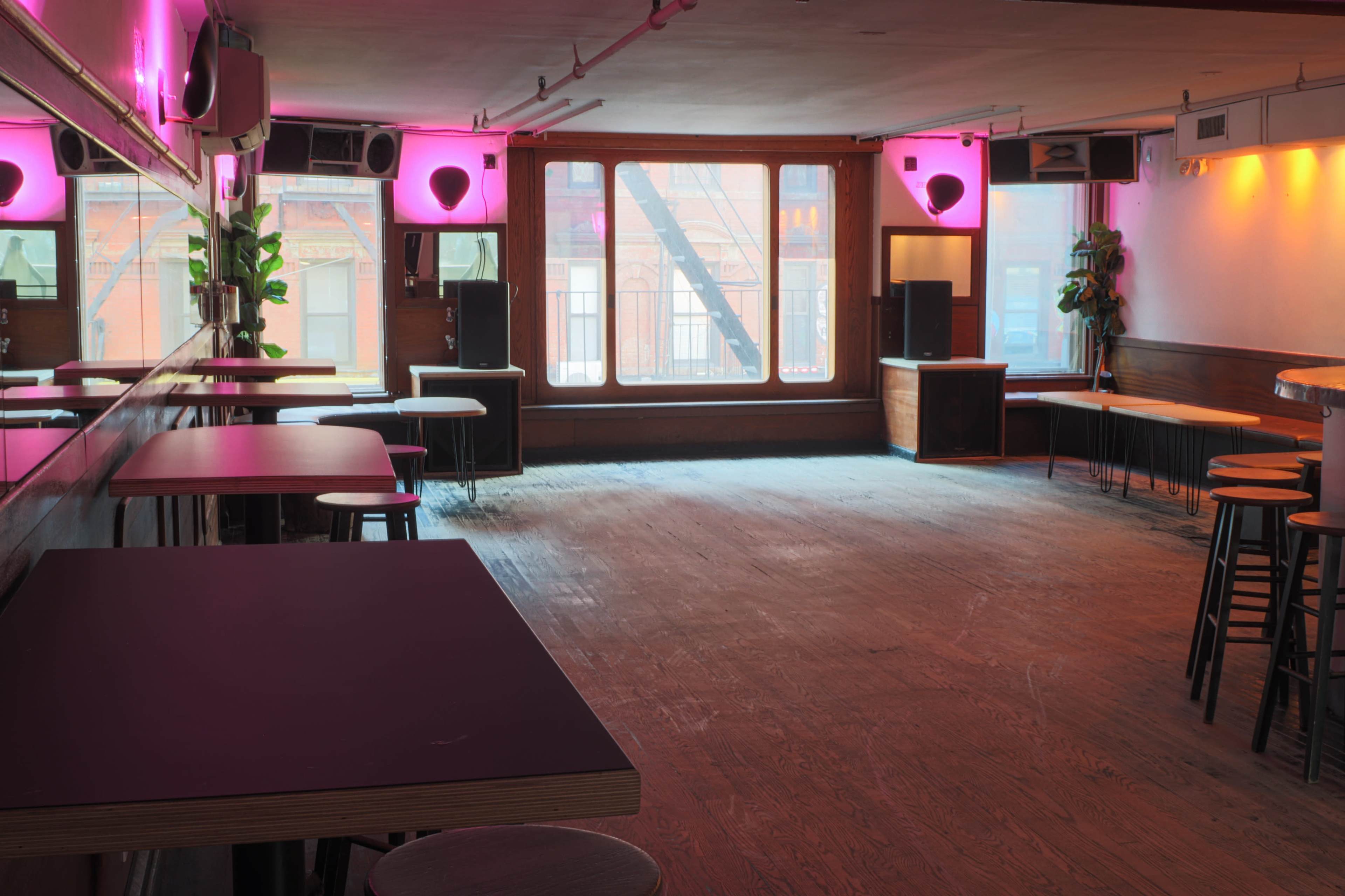 An empty bar or lounge area with wooden floors, minimal furniture, and purple lighting.