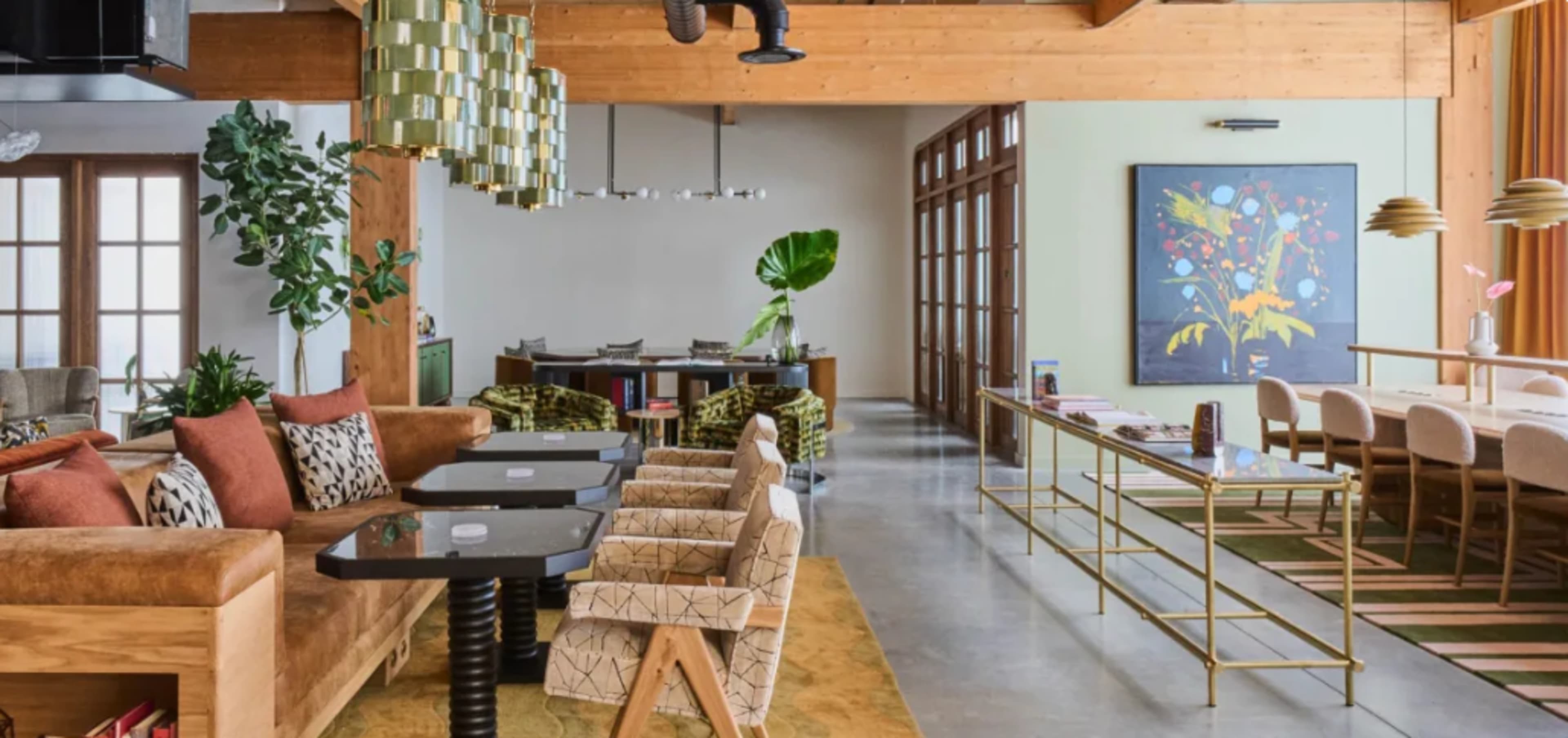 A modern indoor space featuring a blend of seating areas with wooden beams, potted plants, and decorative artwork.