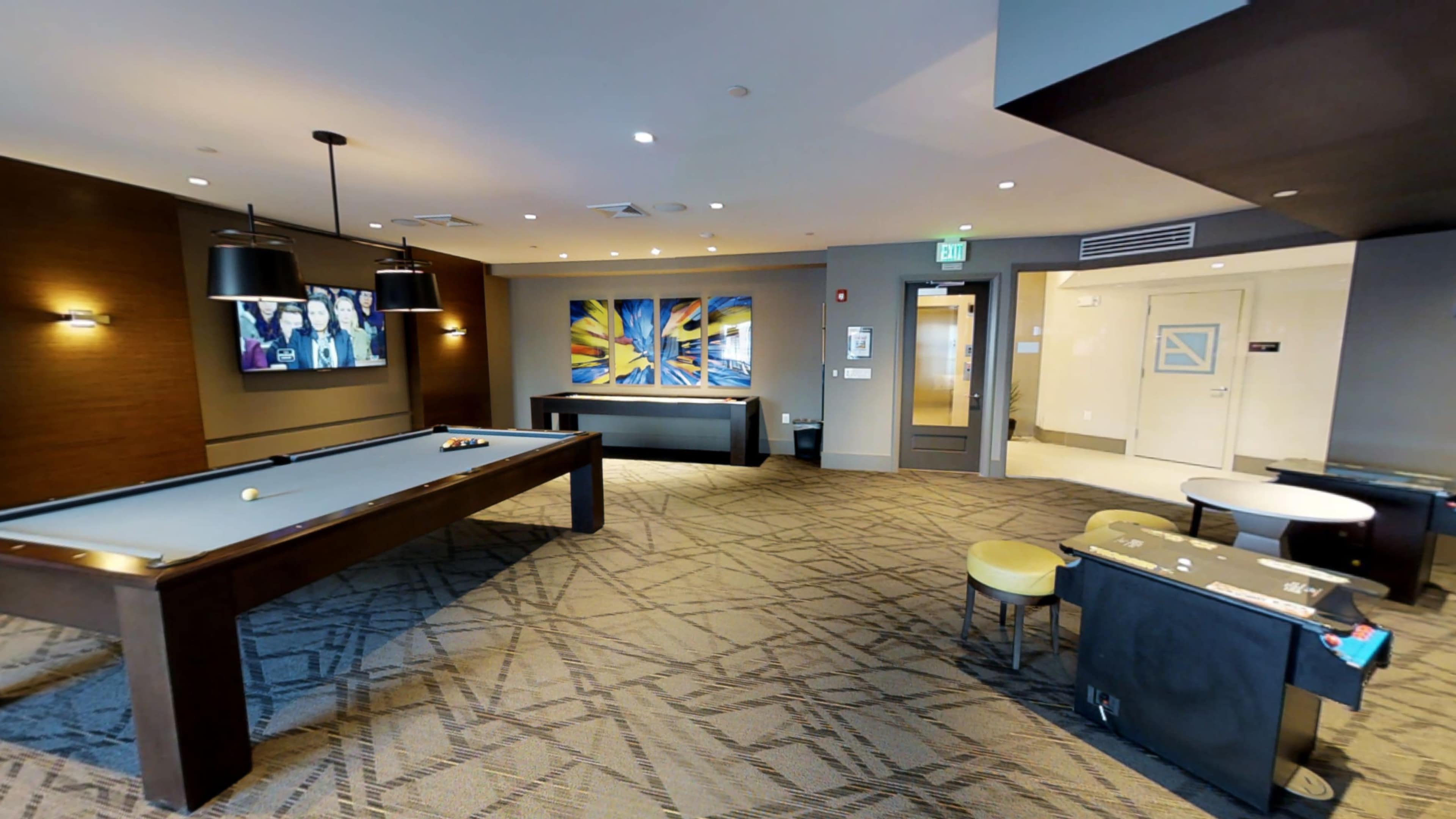 The scene features a game room with a pool table, modern artwork on the walls, and seating areas illuminated by overhead lights.