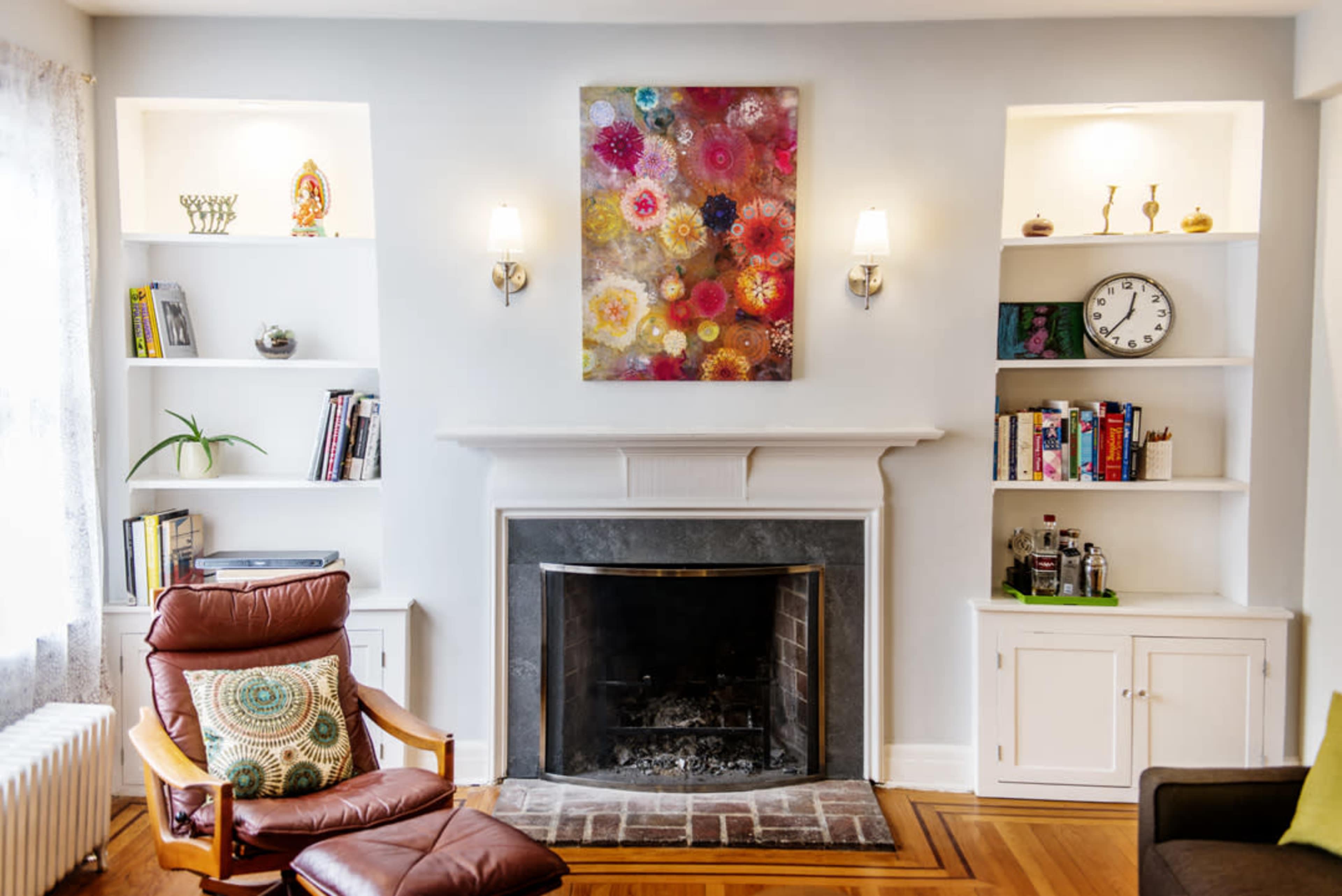 The image shows a living room with a fireplace, framed by built-in shelves displaying books and decorative items, alongside a brown armchair with a patterned cushion.