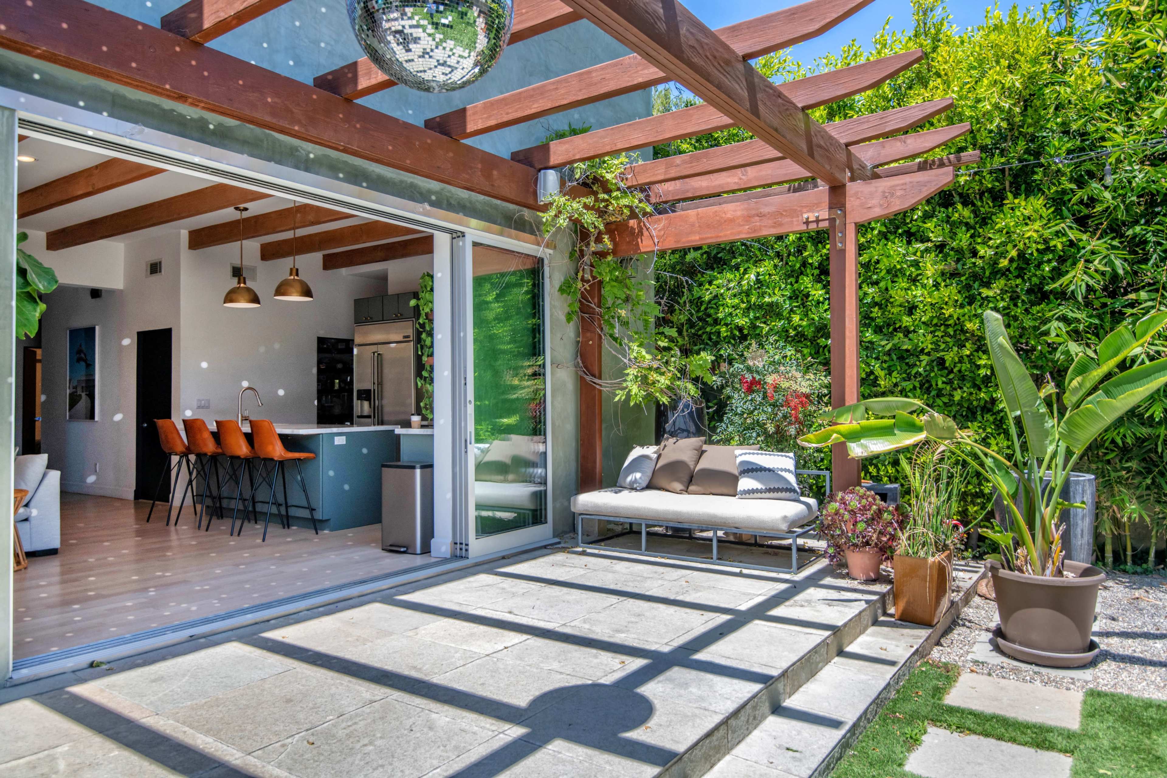 A modern outdoor patio area with a disco ball hanging above a seating arrangement, surrounded by lush greenery and stone pathways.