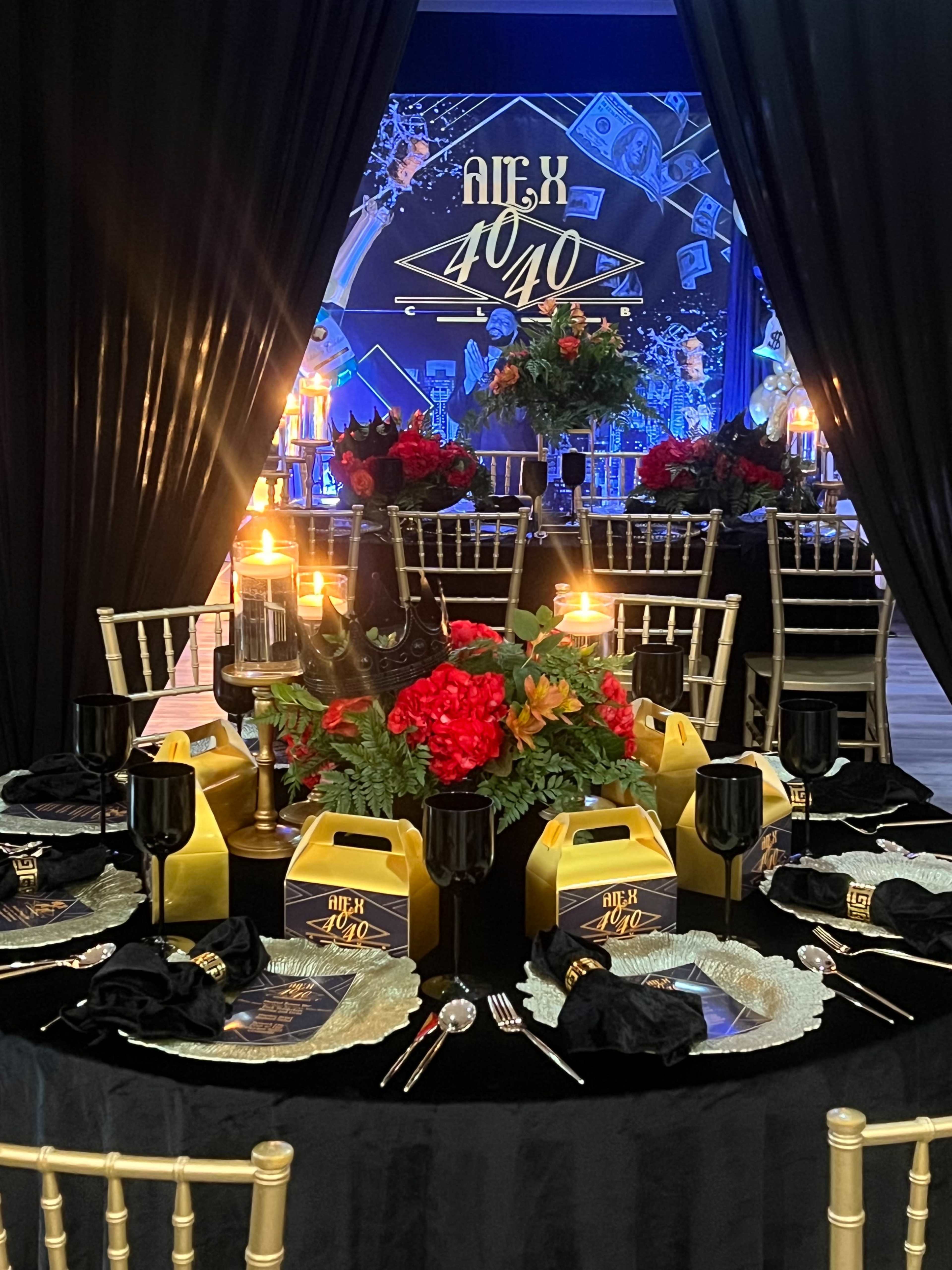 A lavishly decorated dining table features golden takeout boxes, black plates, and vibrant floral arrangements, set against a backdrop of blue and gold decorations.