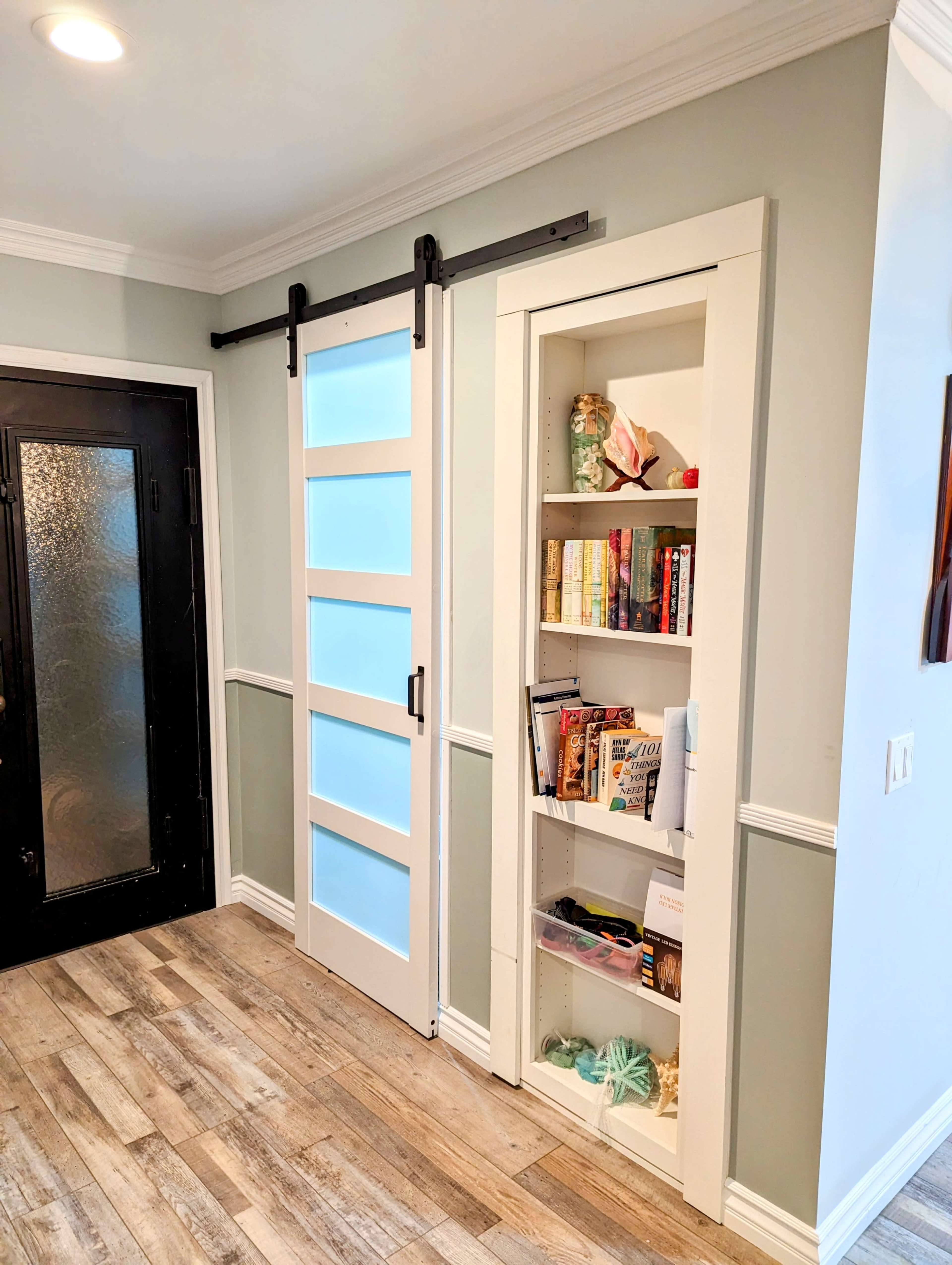 The image shows a hallway featuring a sliding barn door next to a built-in bookshelf filled with various books and decorative items.