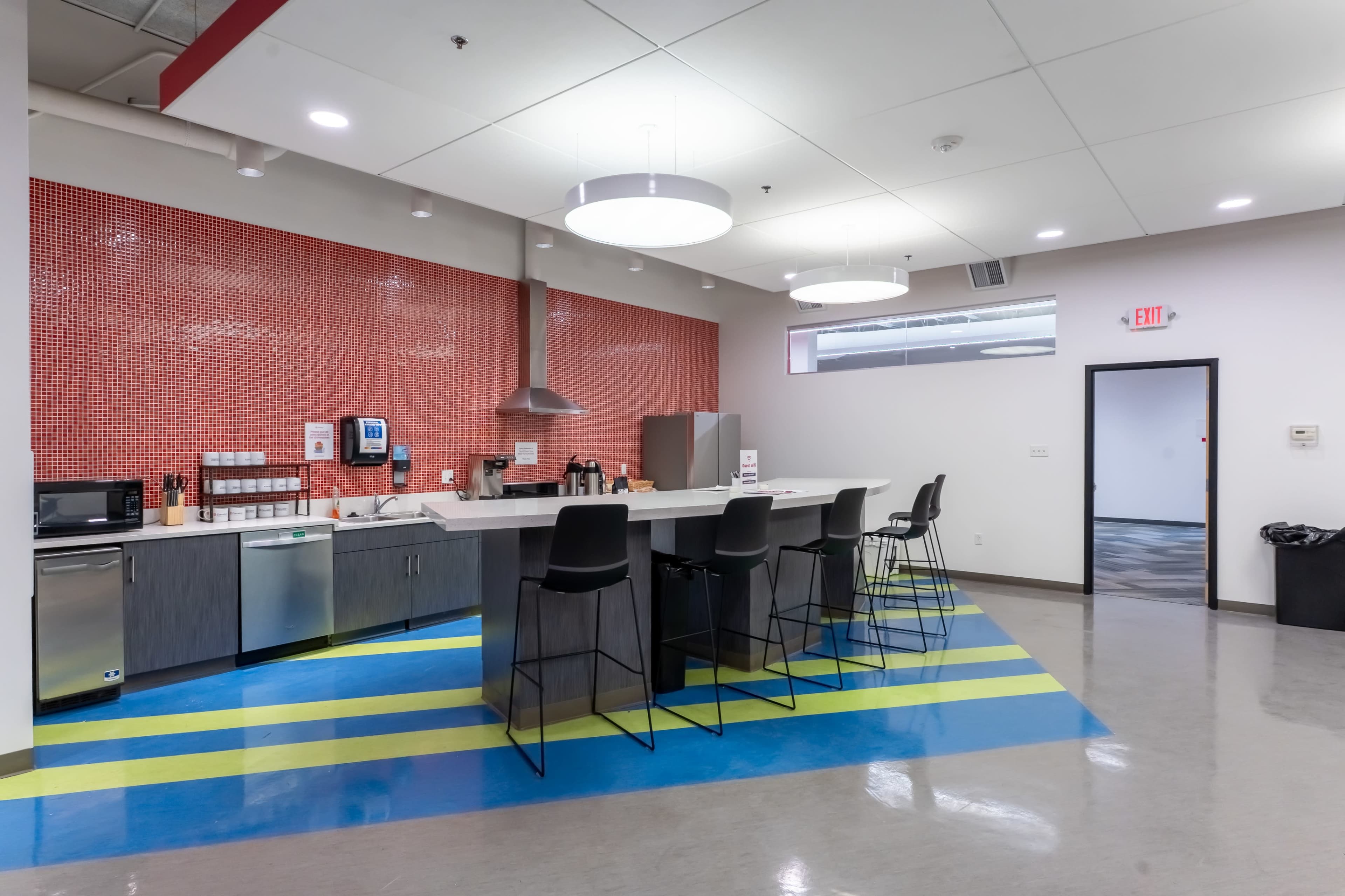 The image shows a modern kitchen area with a long countertop, bar stools, and red mosaic tile on the wall.
