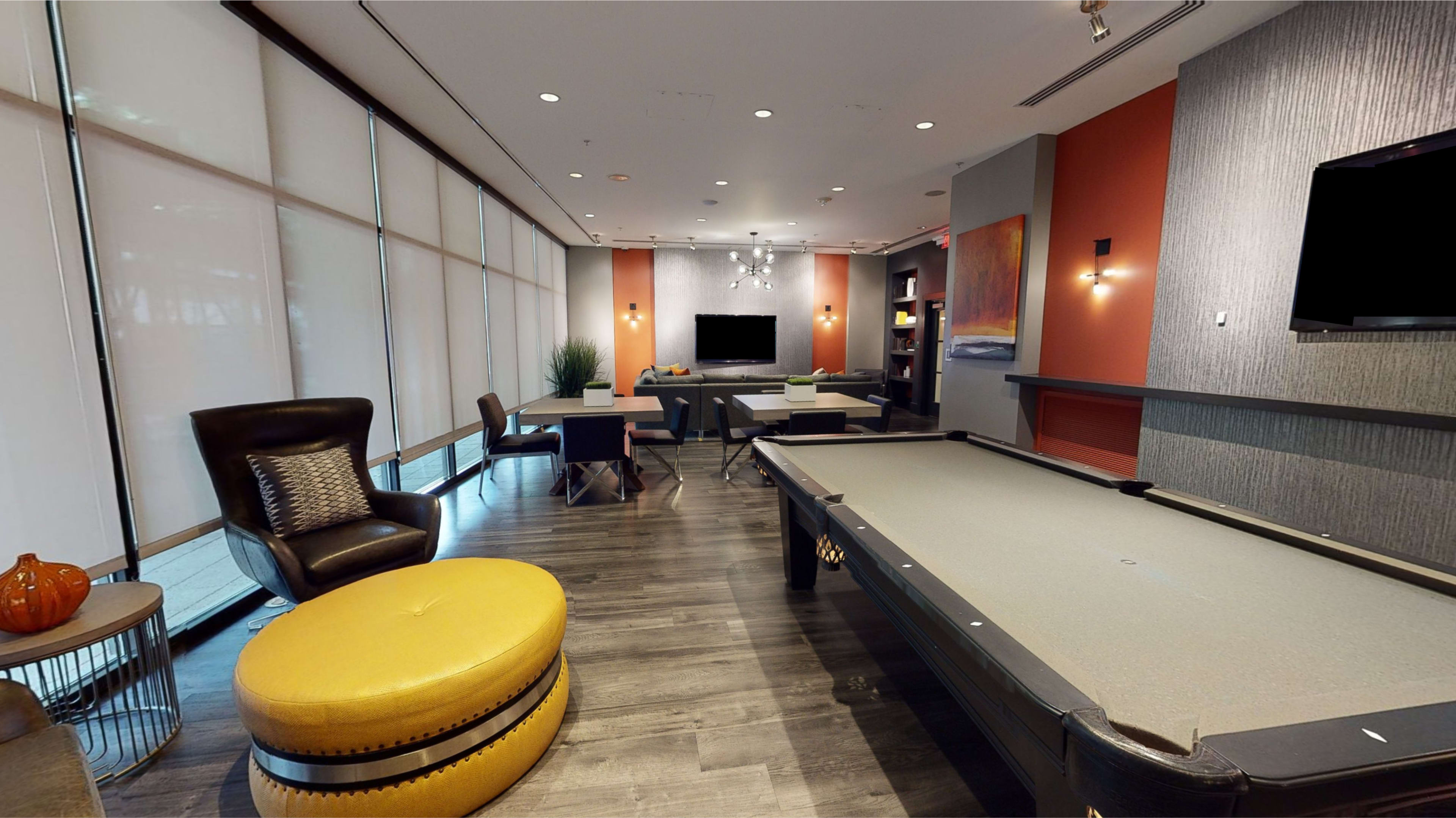 A modern lounge area with a pool table, seating options, and large windows allowing natural light to enter.