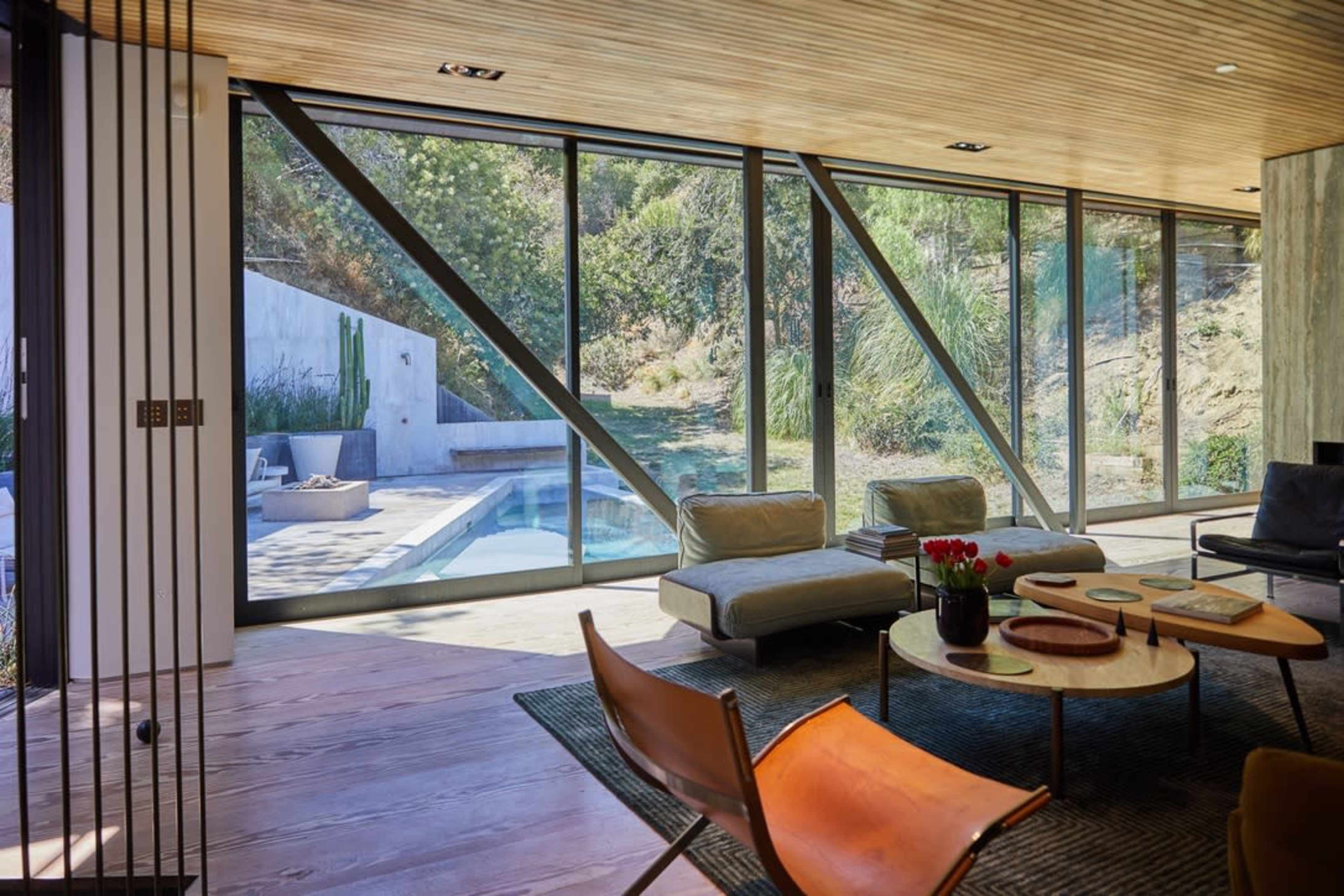 The image shows a modern living room with large glass windows that overlook a backyard featuring a swimming pool and greenery.
