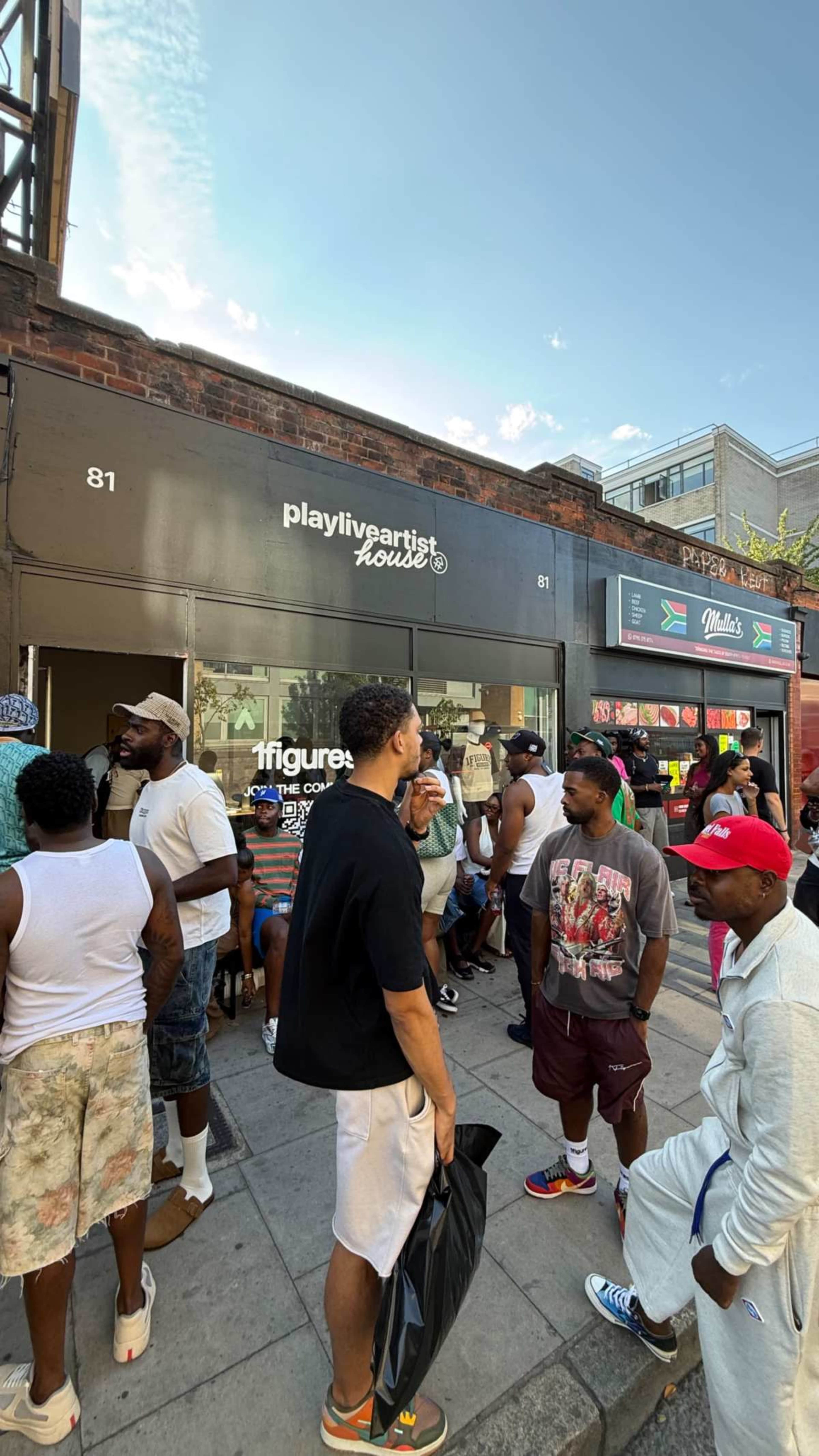 A group of people stands outside the "playliveloverhouse" storefront on a busy street, with a clear blue sky above.