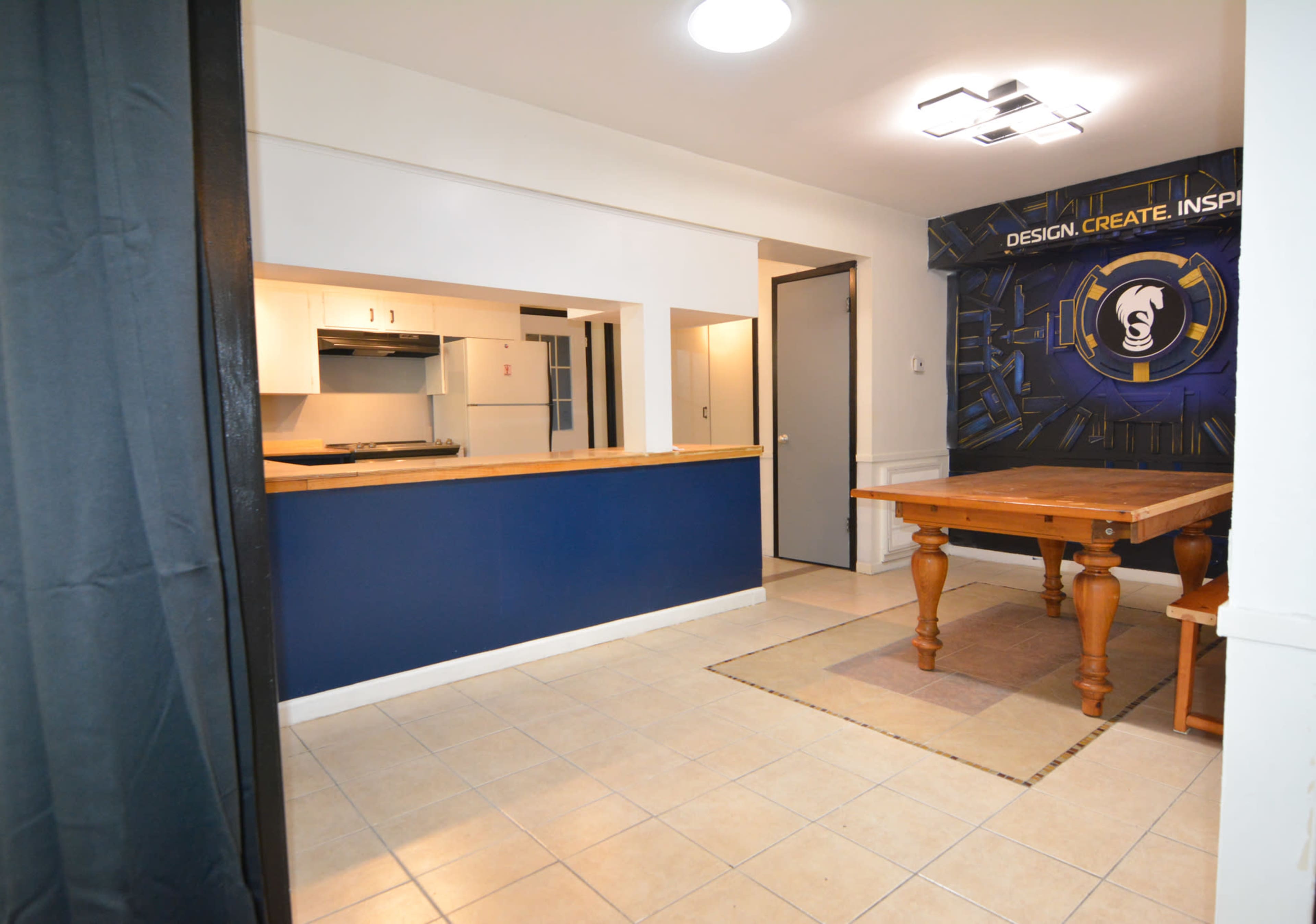A spacious kitchen area featuring a blue accent wall, a wooden dining table, and tiled flooring.