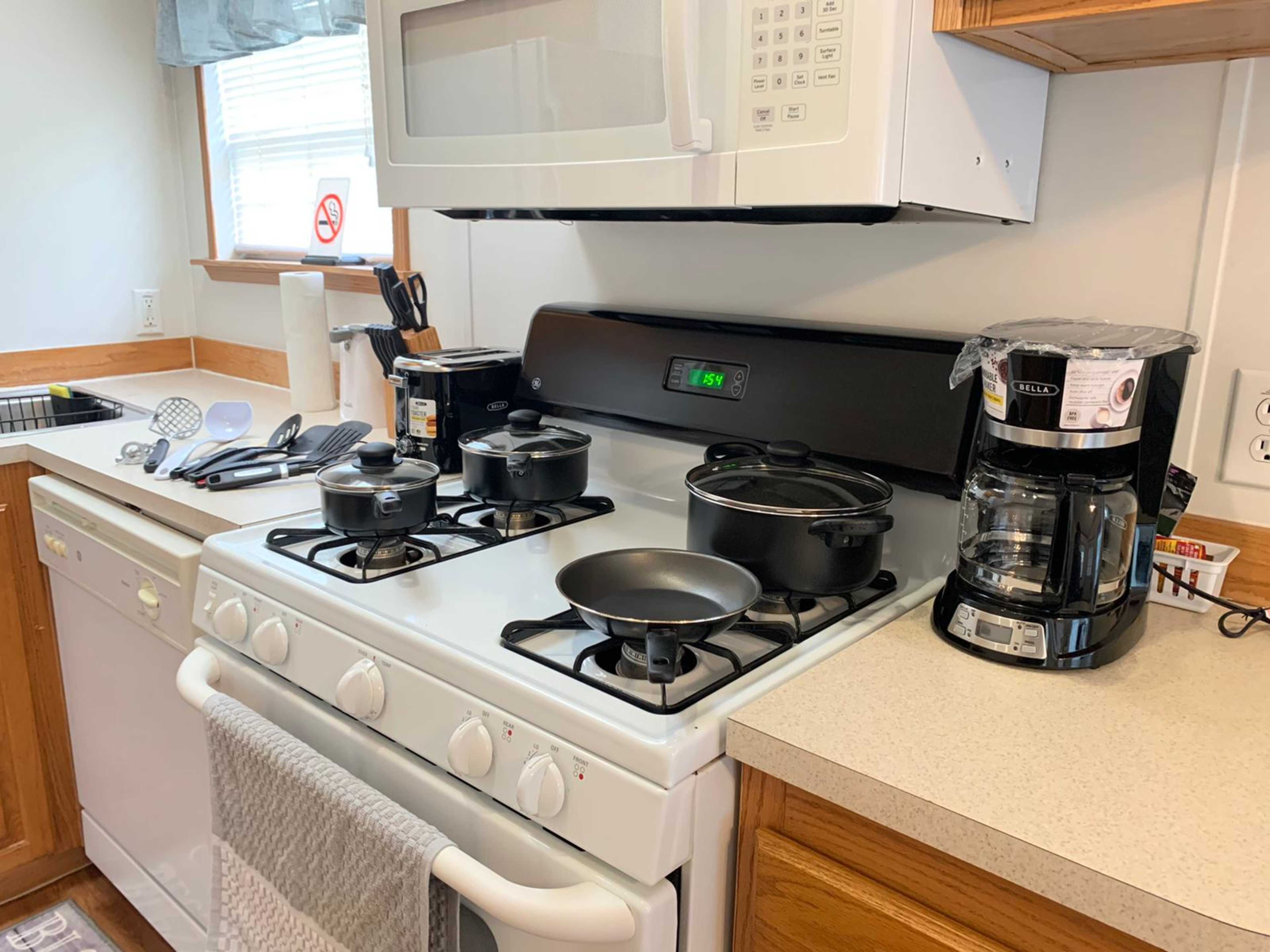 A kitchen with a gas stove, multiple pots and pans on the burners, a coffee maker on the counter, and a microwave above.