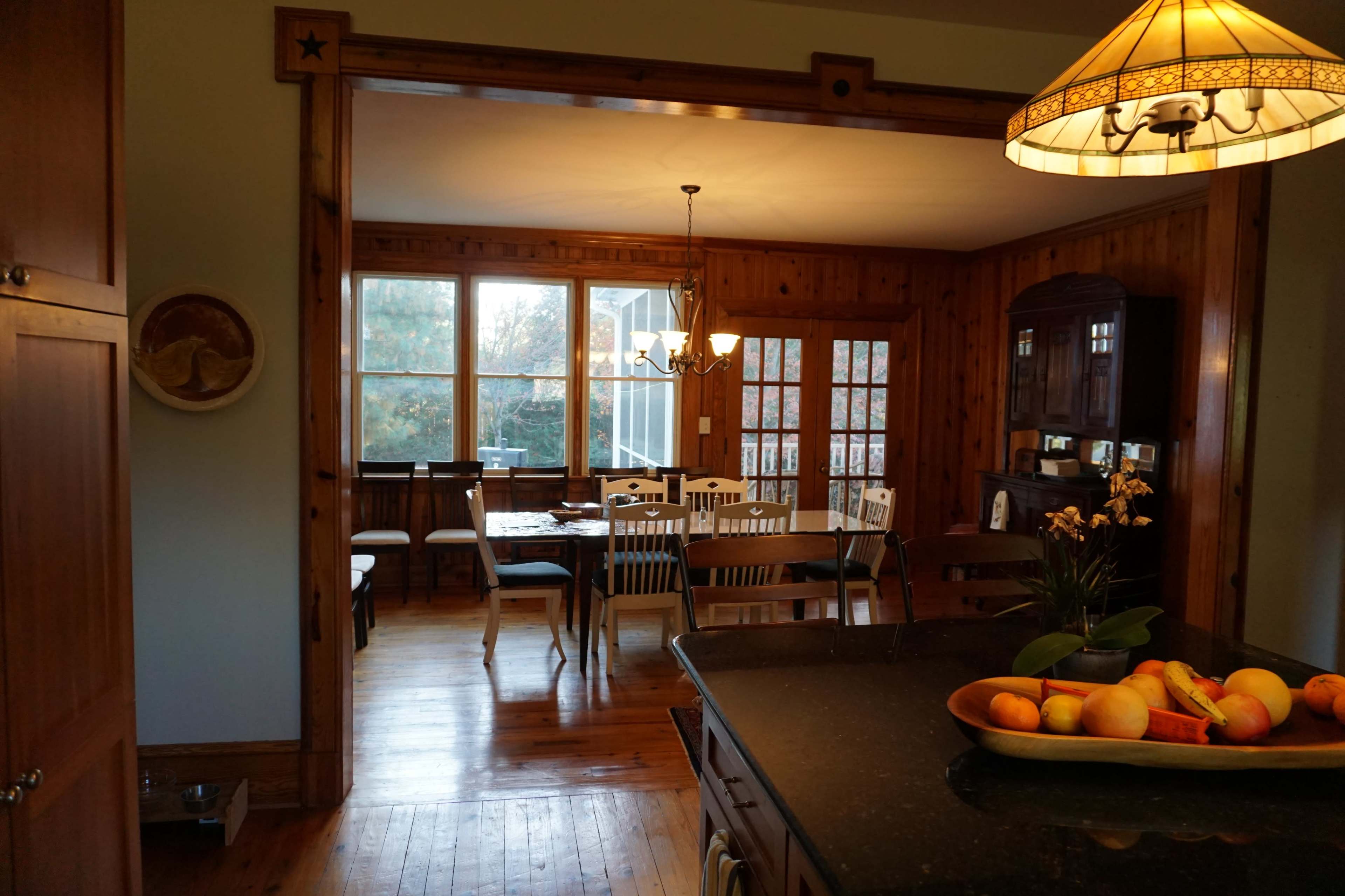 A wooden-furnished kitchen opens into a dining area with a table set for several people.
