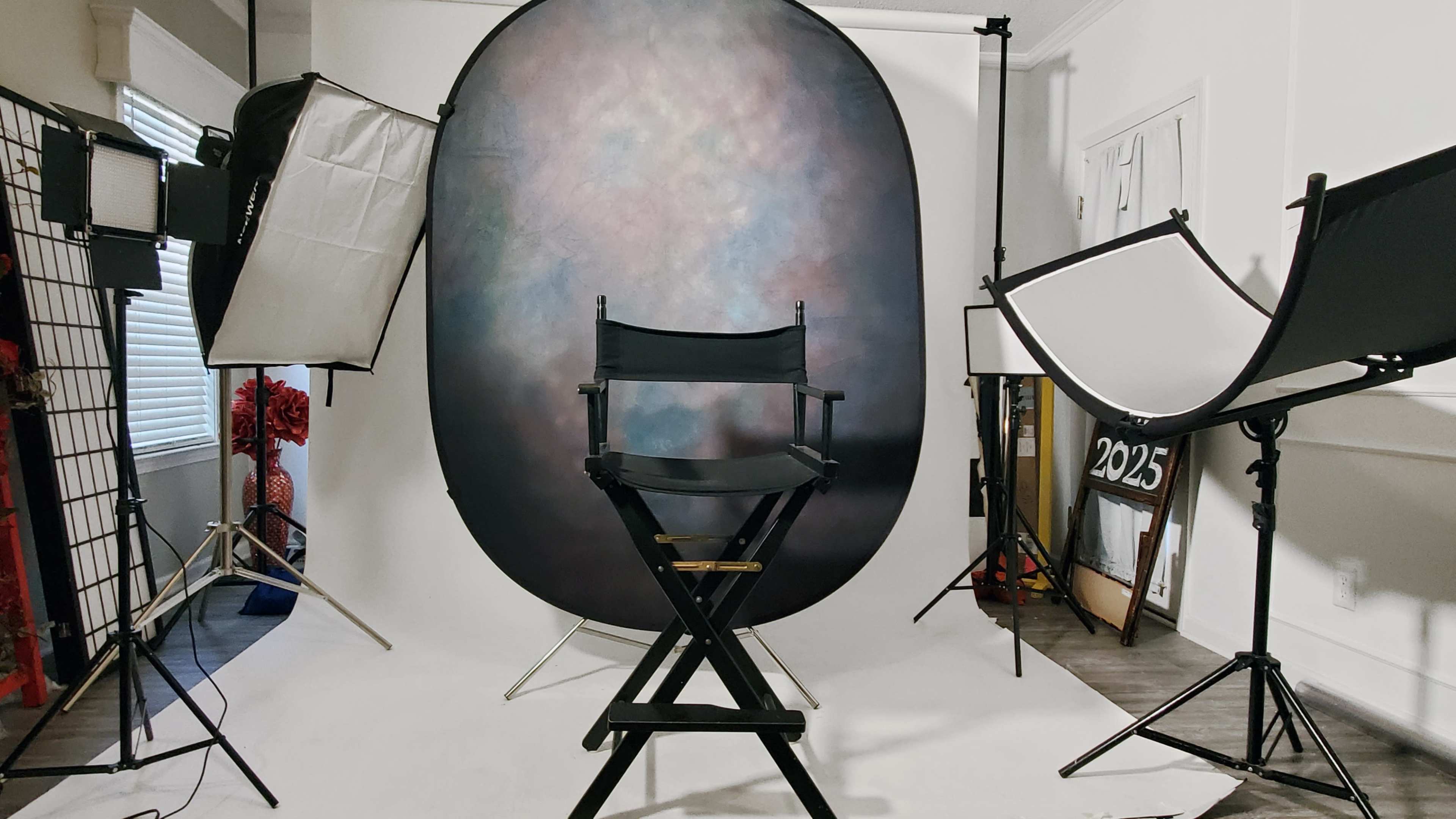 A photography studio is set up with a director's chair in front of a backdrop and various lighting equipment.