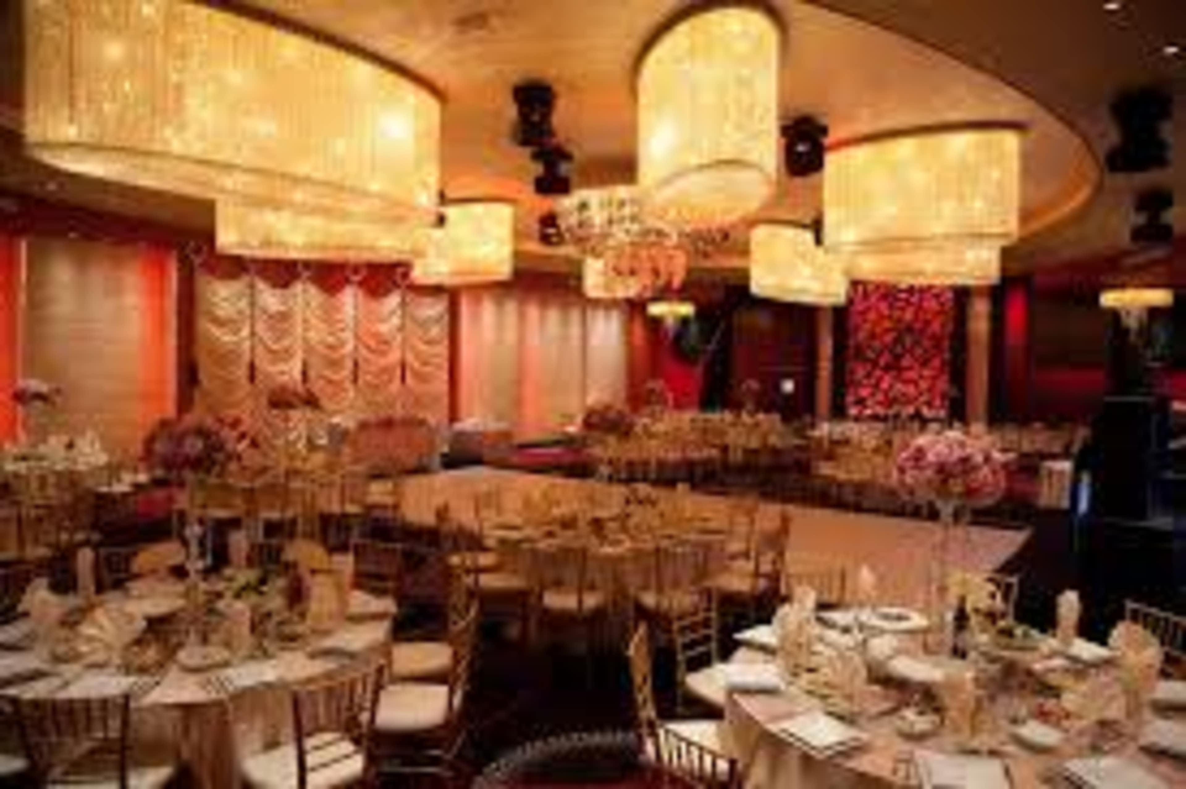 An elegantly arranged banquet hall with round tables set for dining, adorned with floral centerpieces, and illuminated by large chandeliers.