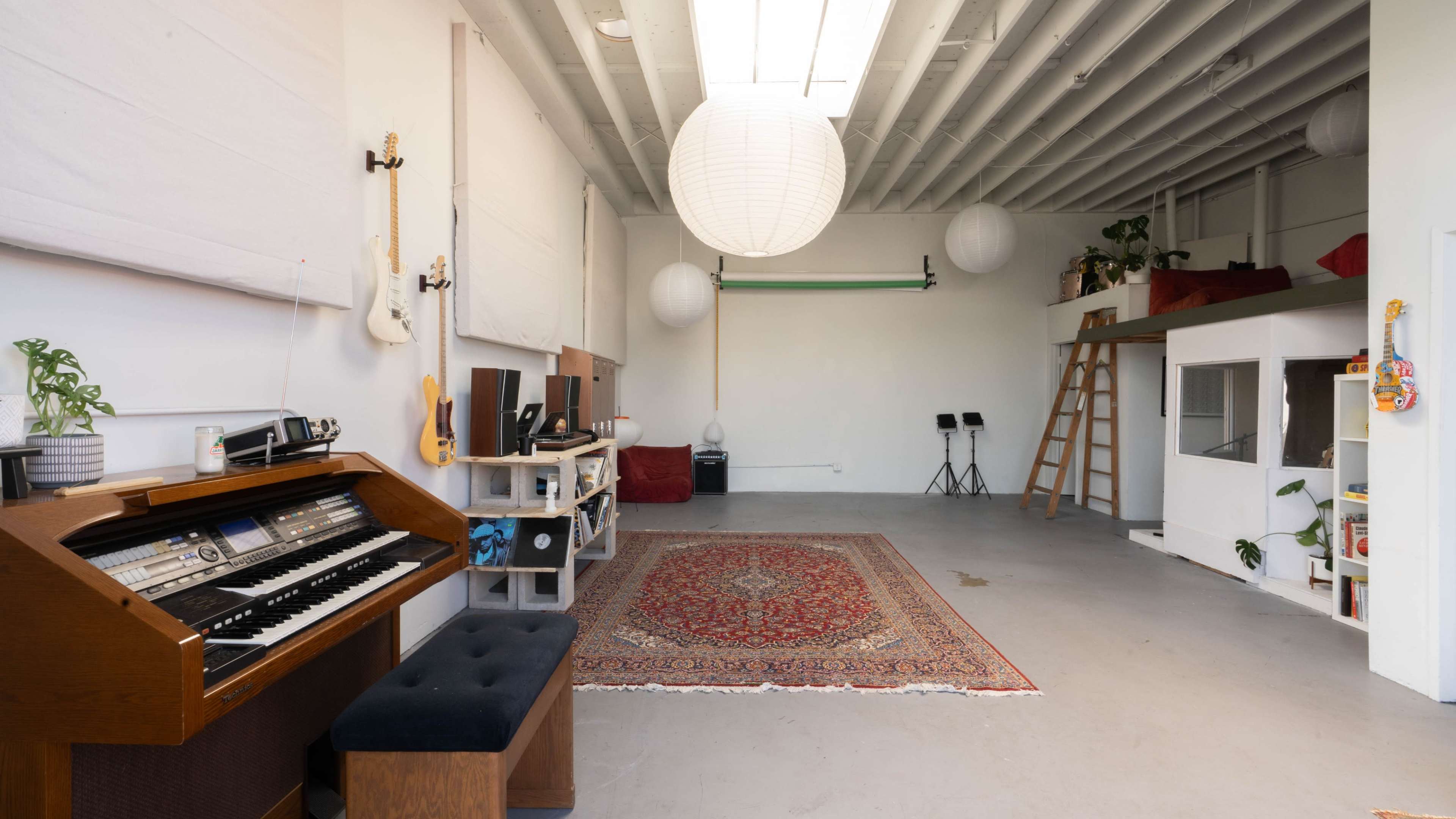 A spacious room features an organ, a large rug, and various musical instruments, with hanging lanterns and a ladder leading to a loft area.