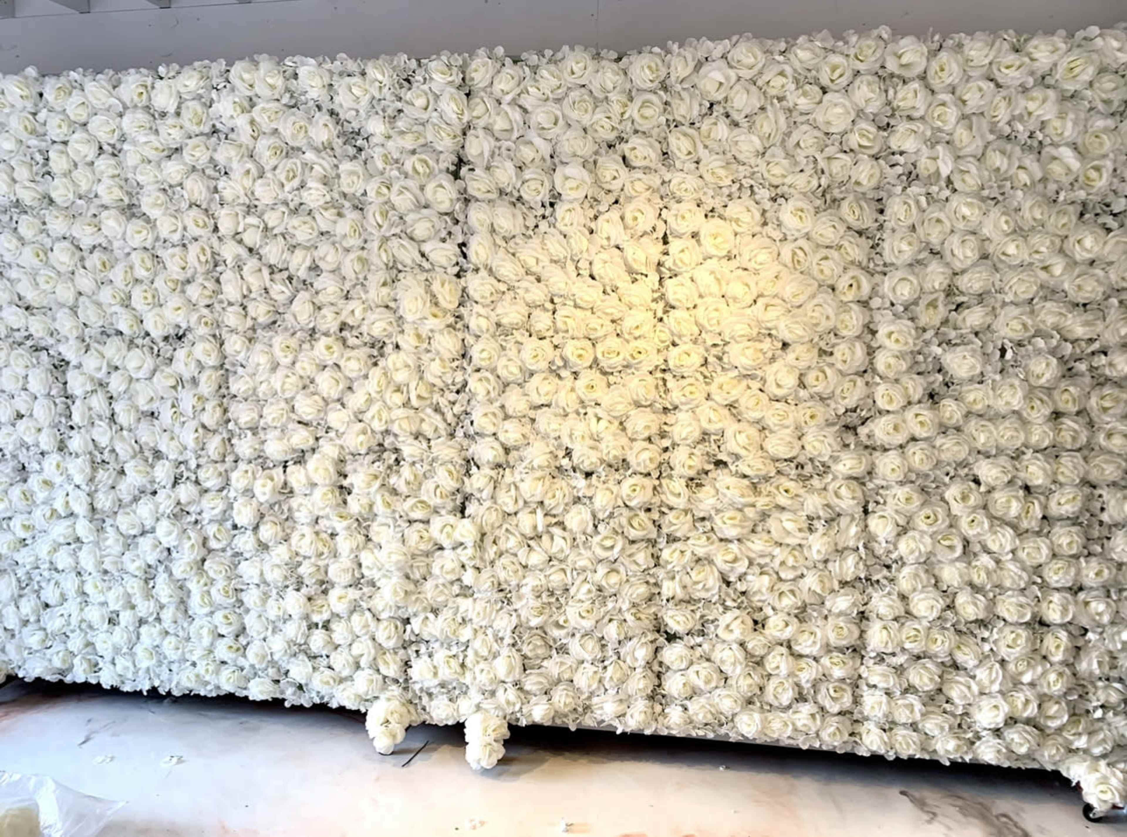 The image shows a large wall covered entirely with artificial white roses.
