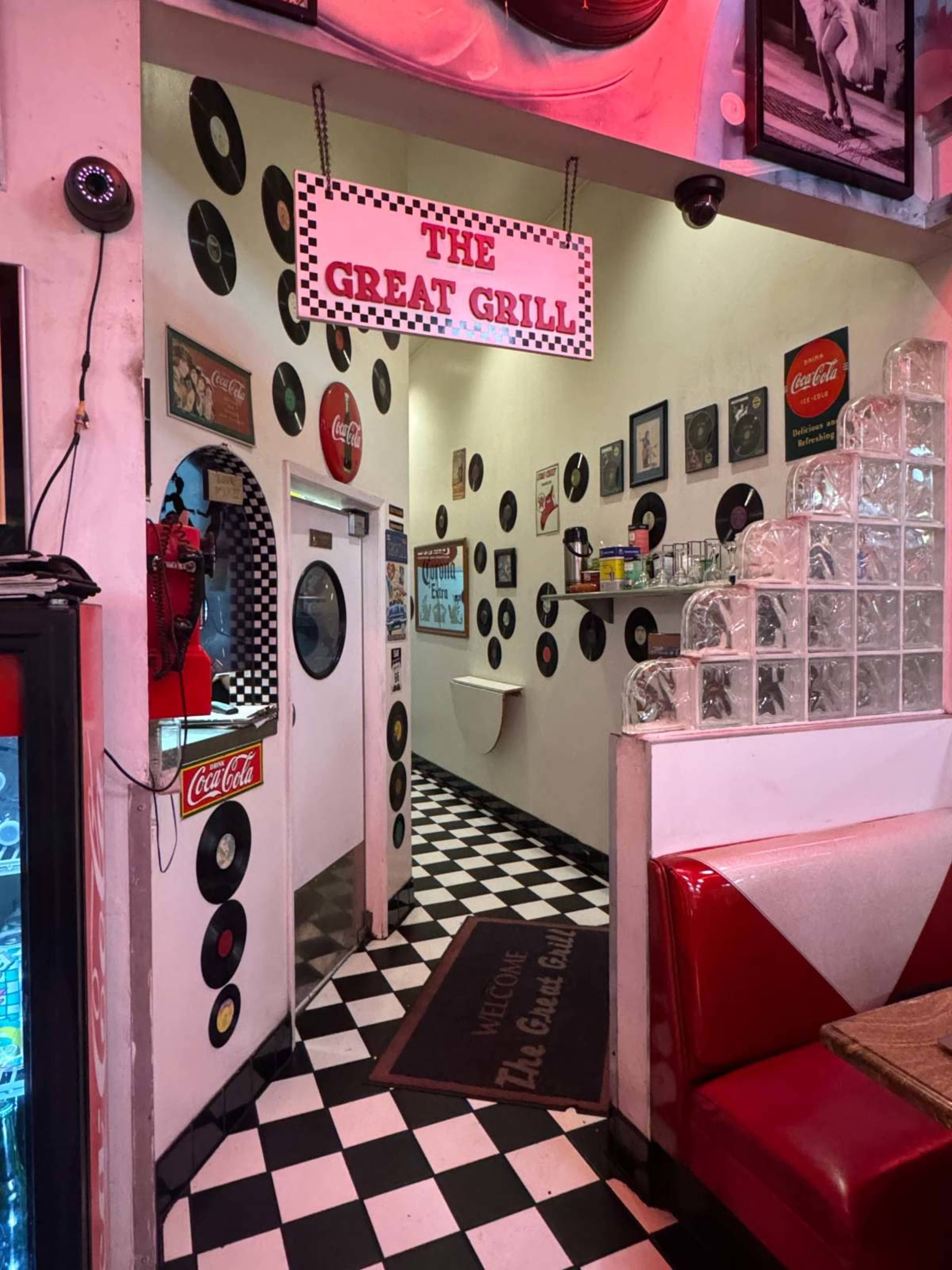 The image shows a retro diner interior featuring black and white checkered flooring, red booths, and walls adorned with vinyl records and vintage signs.