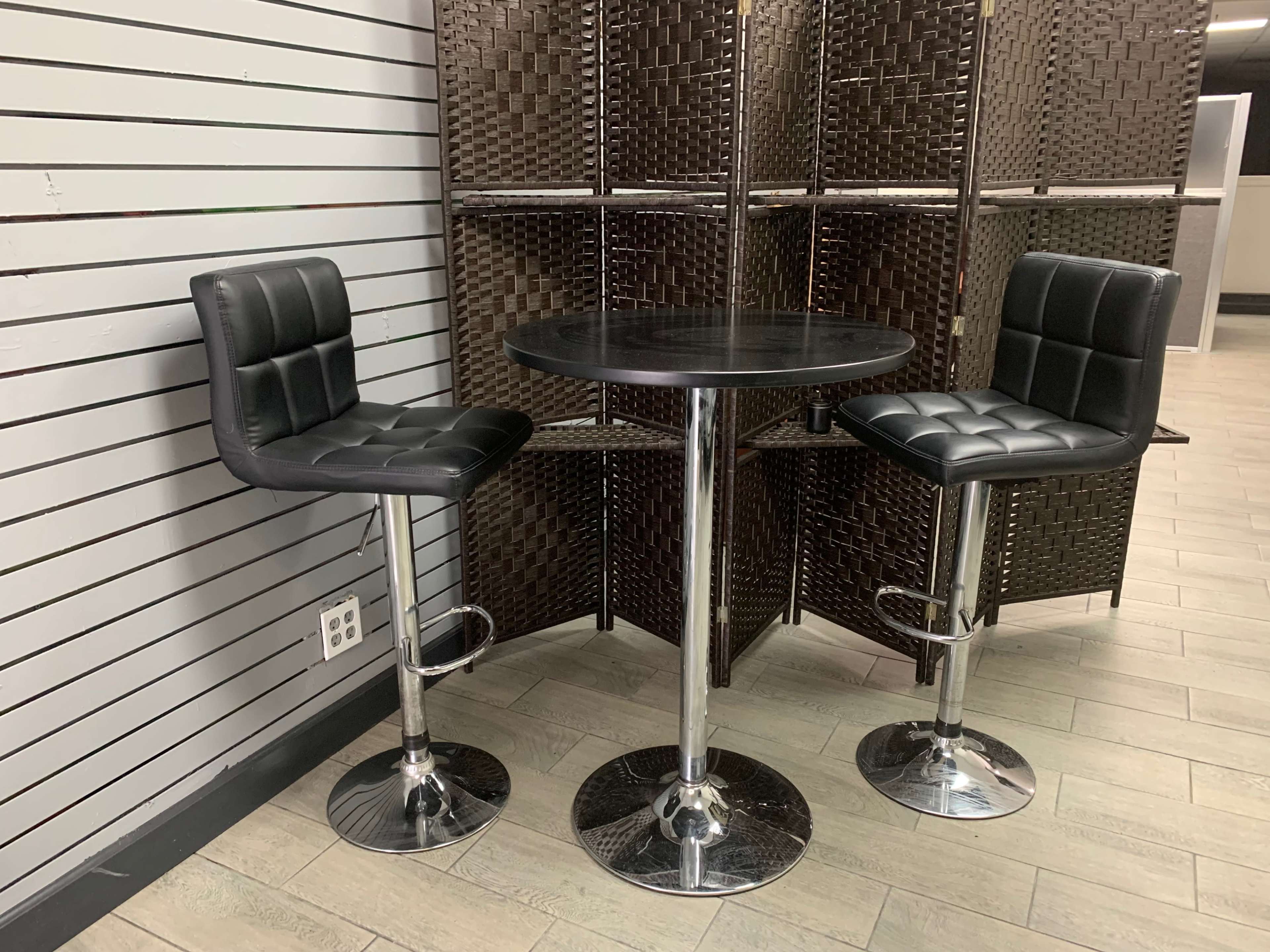 A small black table with two matching bar stools set against a wooden dividing screen in a room with striped walls.